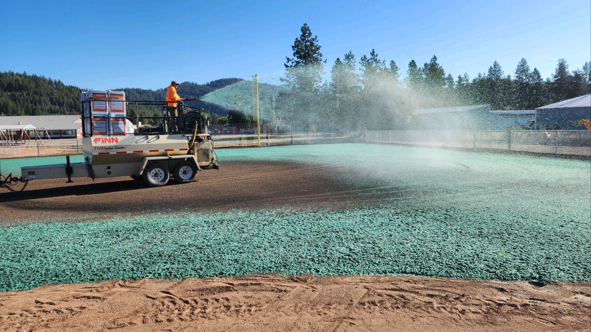 Hydroseeding machine spraying green mixture on ground for lawn establishment."}