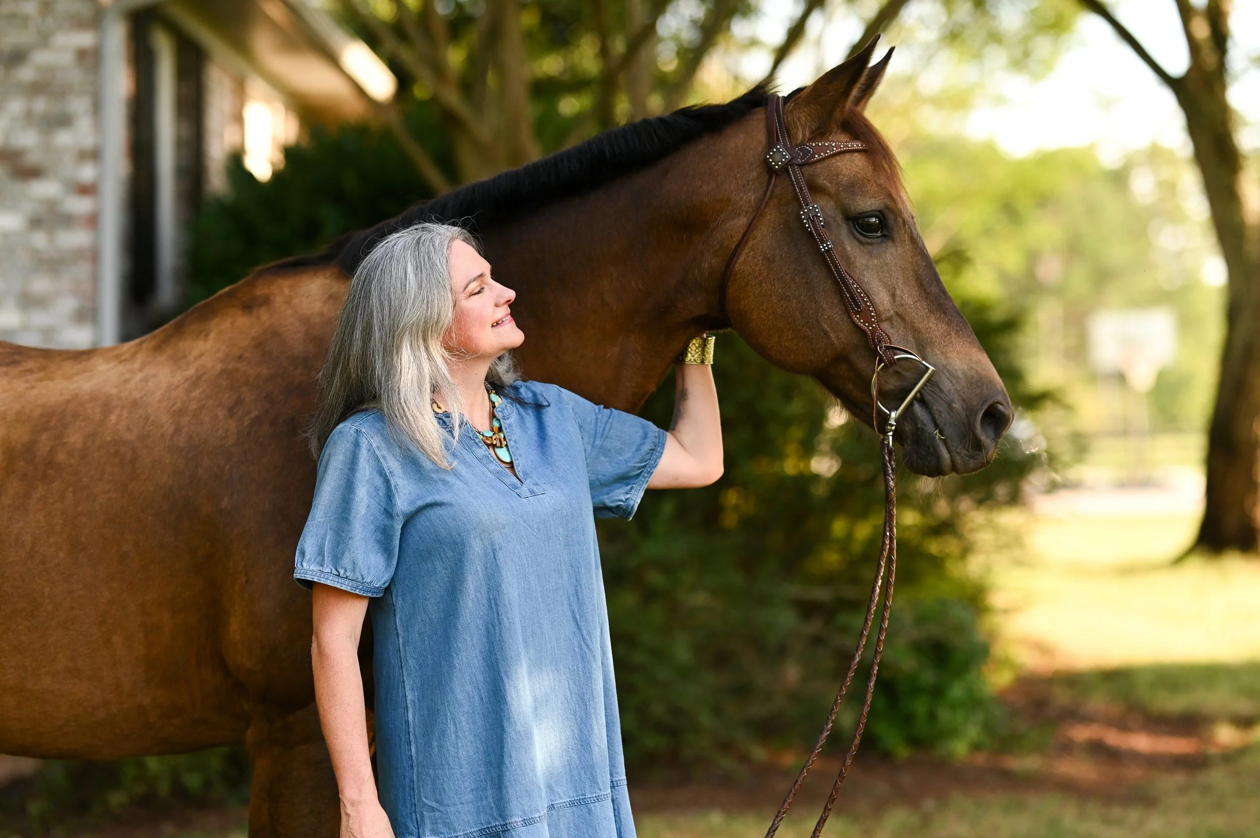 Morgan Brawley, LCMHCA, eyes closed and smiling beside her bay horse