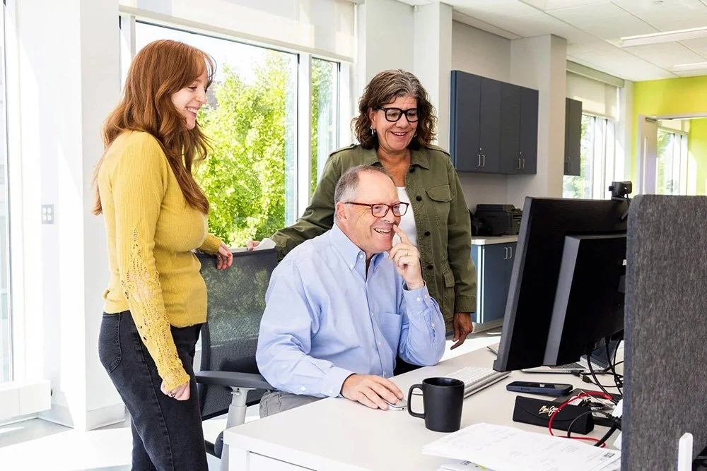 Finance team of three smile while looking at computer and assessing client's finances