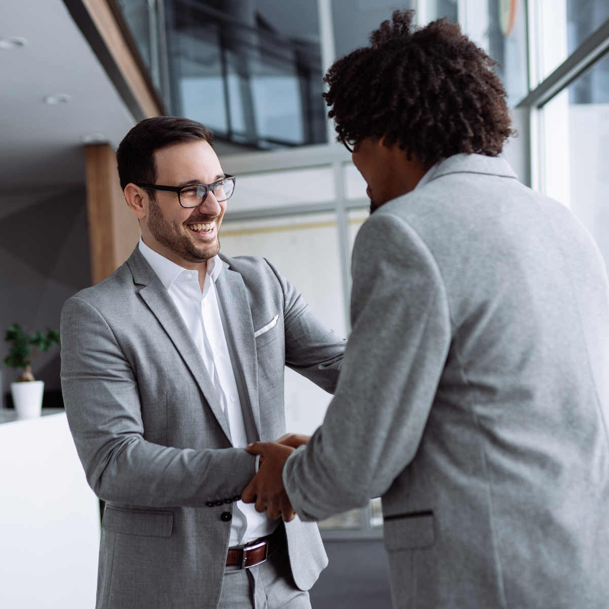 Two corporate employees smiling and shaking hands, representing positive peer-to-peer recognition.
