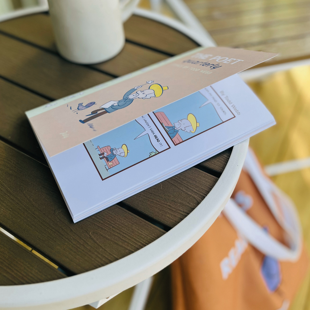 The Poet Quarterly comic book by Todd Webb on a wooden outdoor table, with a white mug and a chair partially visible in the background.