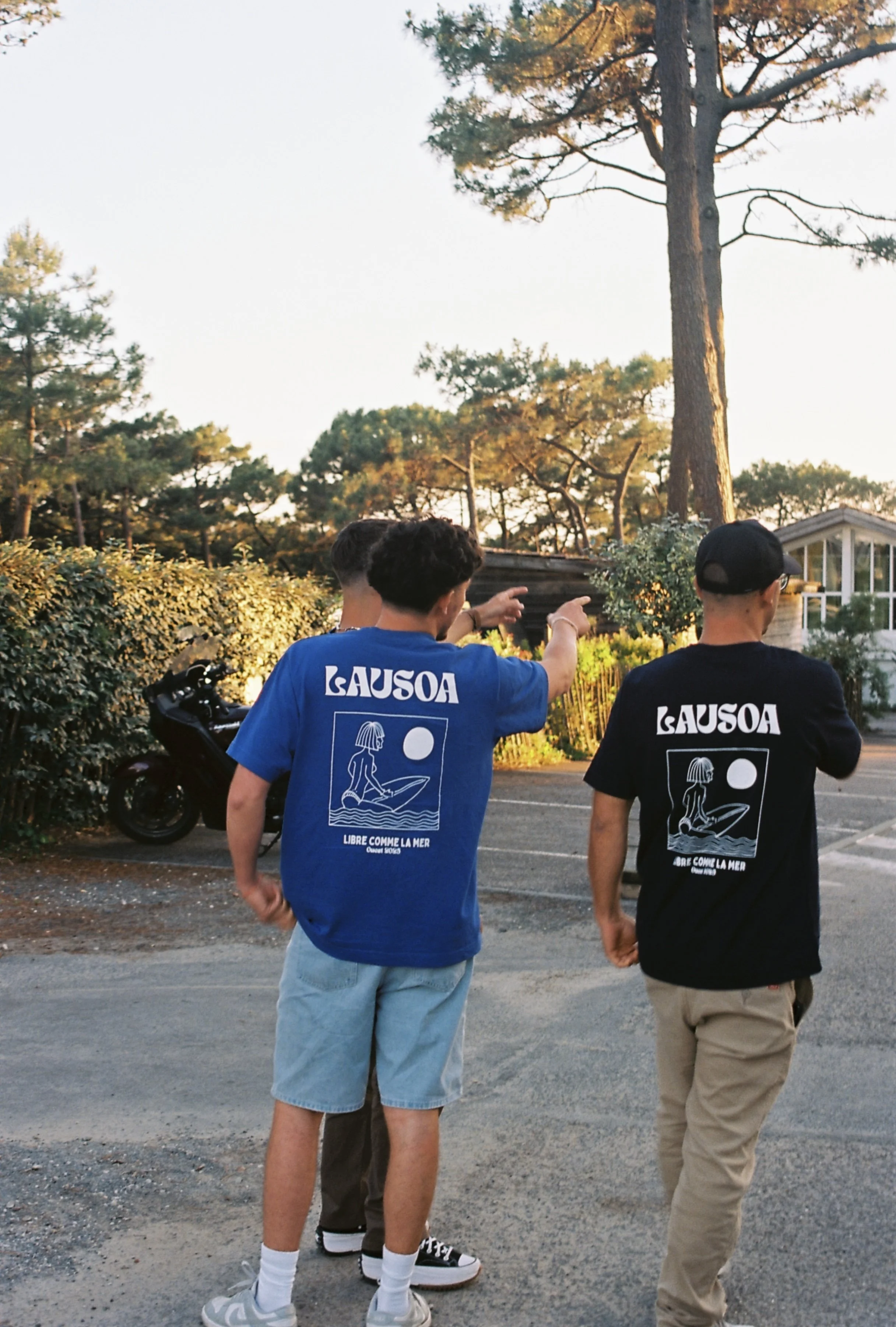 Trois jeunes hommes marchant dehors, portant des t-shirts bleus et noirs avec un dessin de sirène et la phrase "Libre comme la mer".