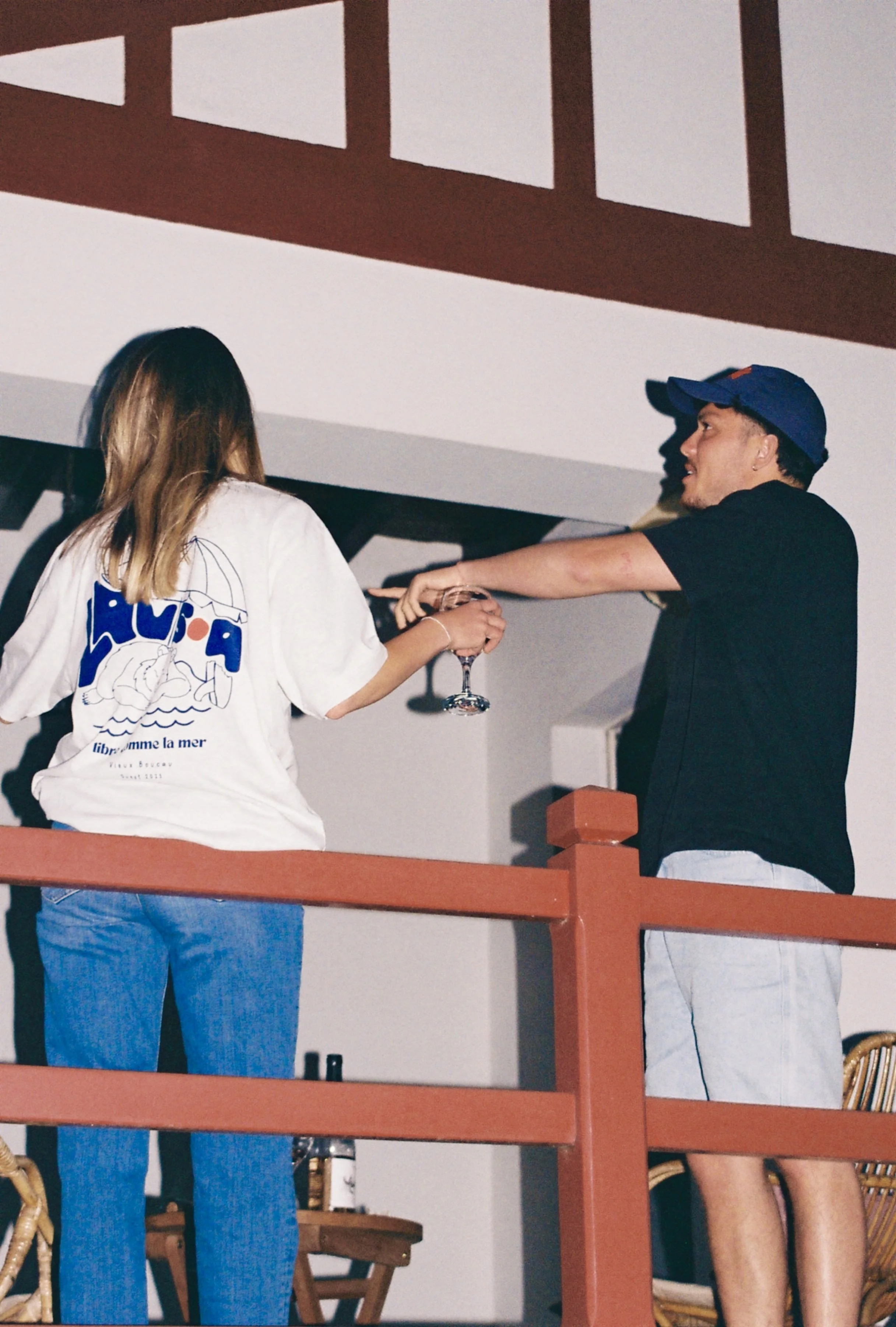 Deux personnes, une femme avec un t-shirt blanc et un homme avec un t-shirt noir, échangent un verre lors d'une fête, en milieu intérieur.