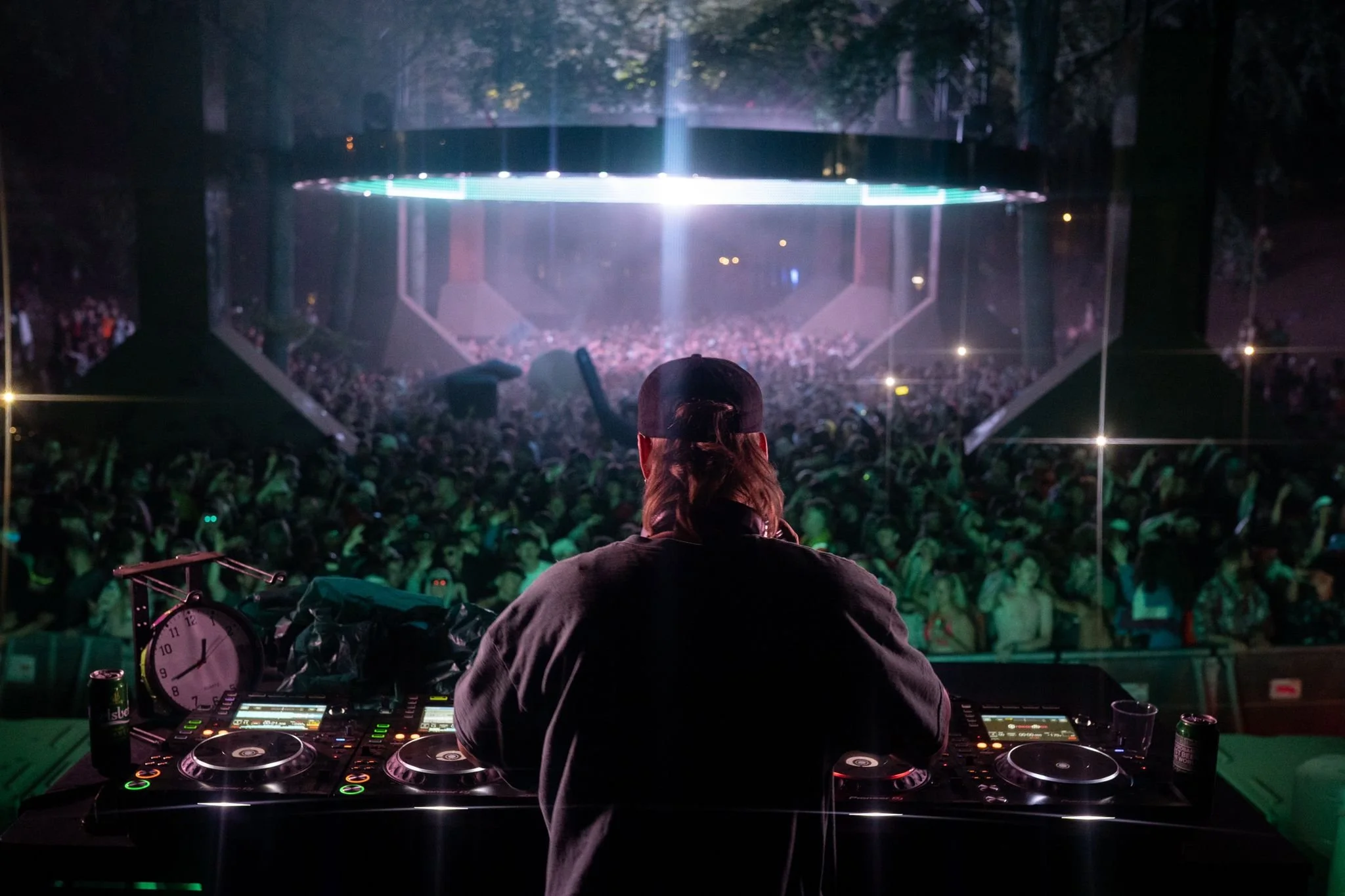 DJ performing on stage at a concert or music festival with a large crowd in front and a digital screen above the stage.