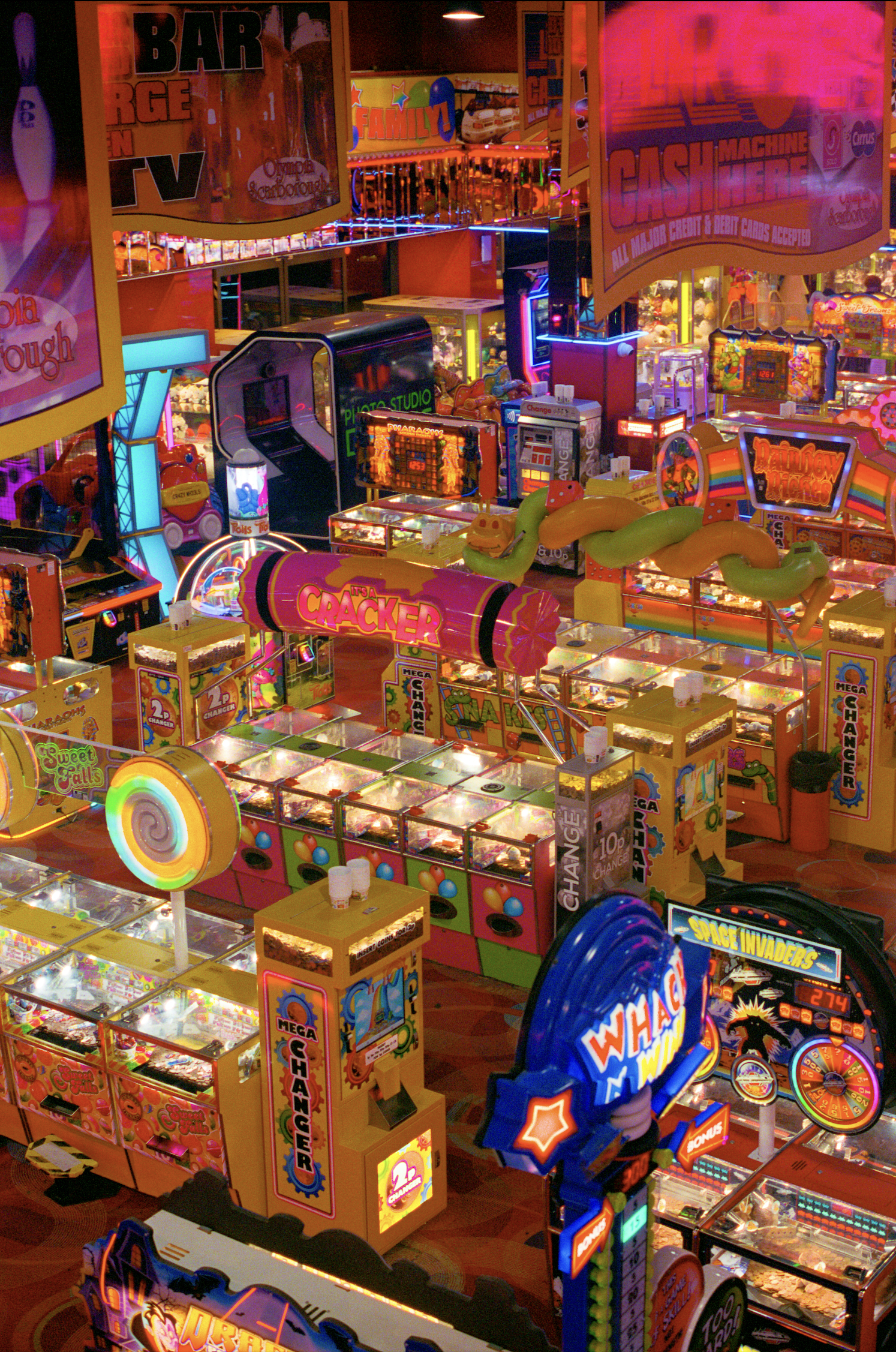 Colorful arcade with various game machines, including claw machines, coin pushers, and bright signage, illuminated by vibrant neon lights.