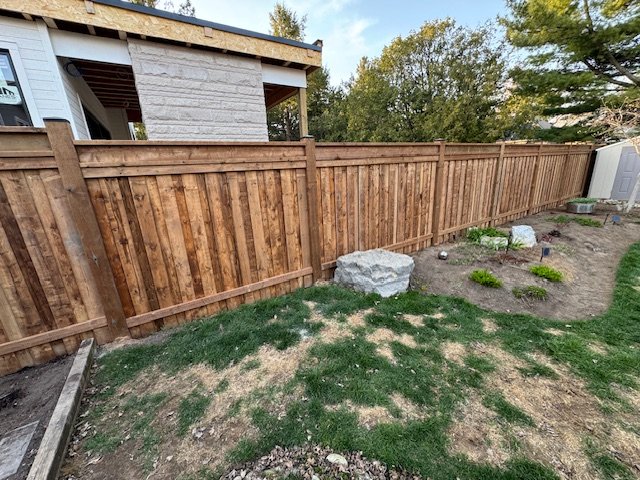 Wooden fence bordering a backyard with grassy and landscaped areas next to a house.