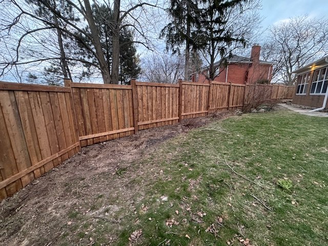 Wooden privacy fence in a backyard with trees and a house nearby.