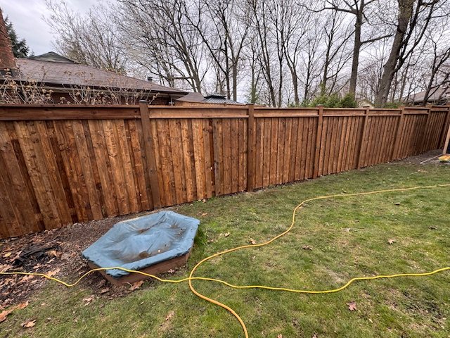 Wooden fence with tarp-covered sandbox and yellow hose on grass