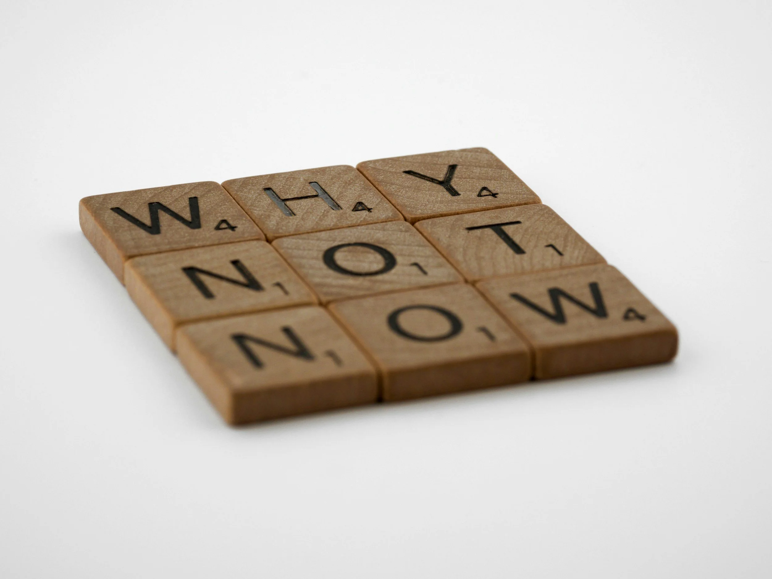 Close-up of wooden Scrabble tiles spelling out the words 'WHY NOT' on a white background.