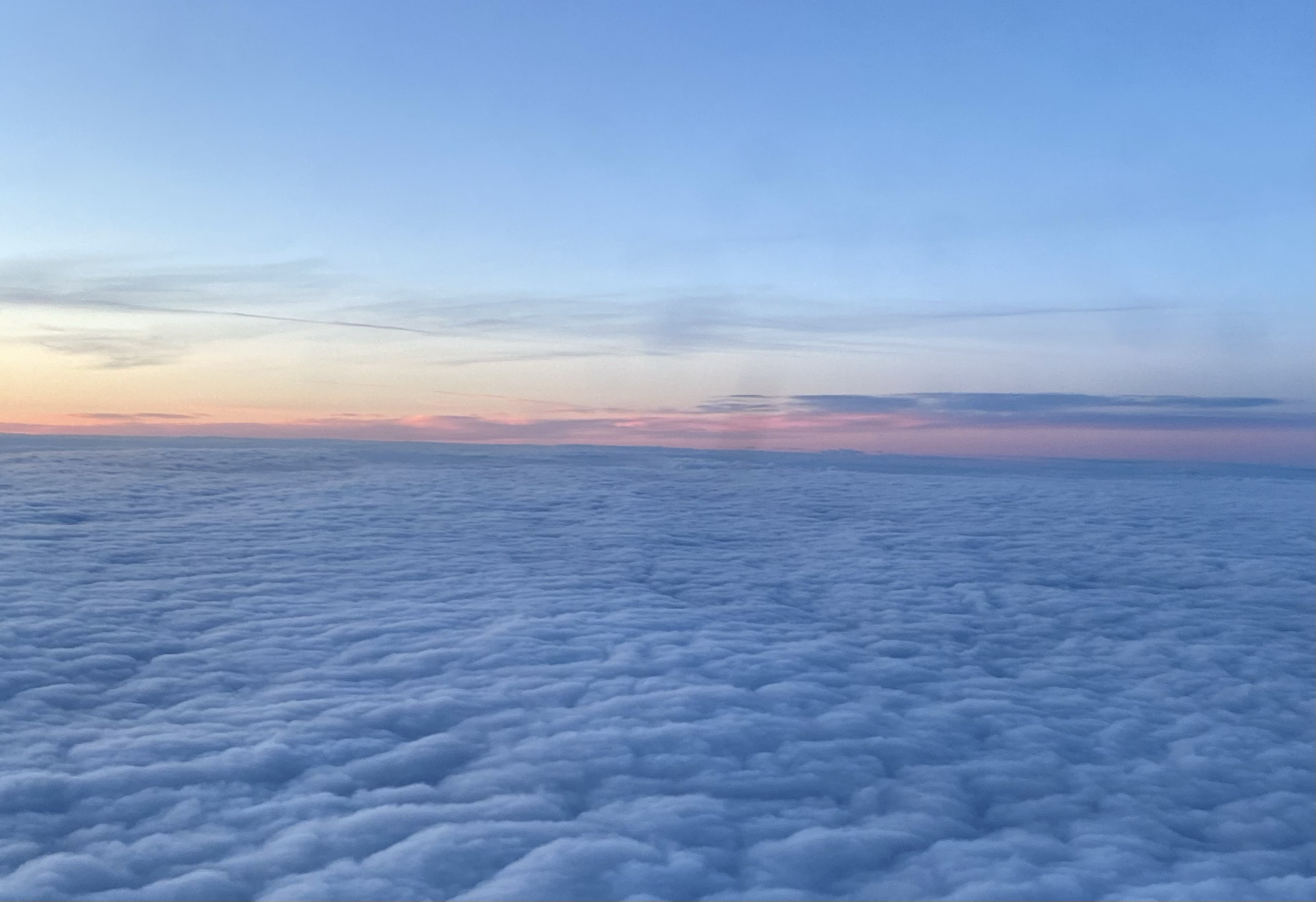 Aerial view of fluffy clouds during sunset with pink and orange hues in the sky.