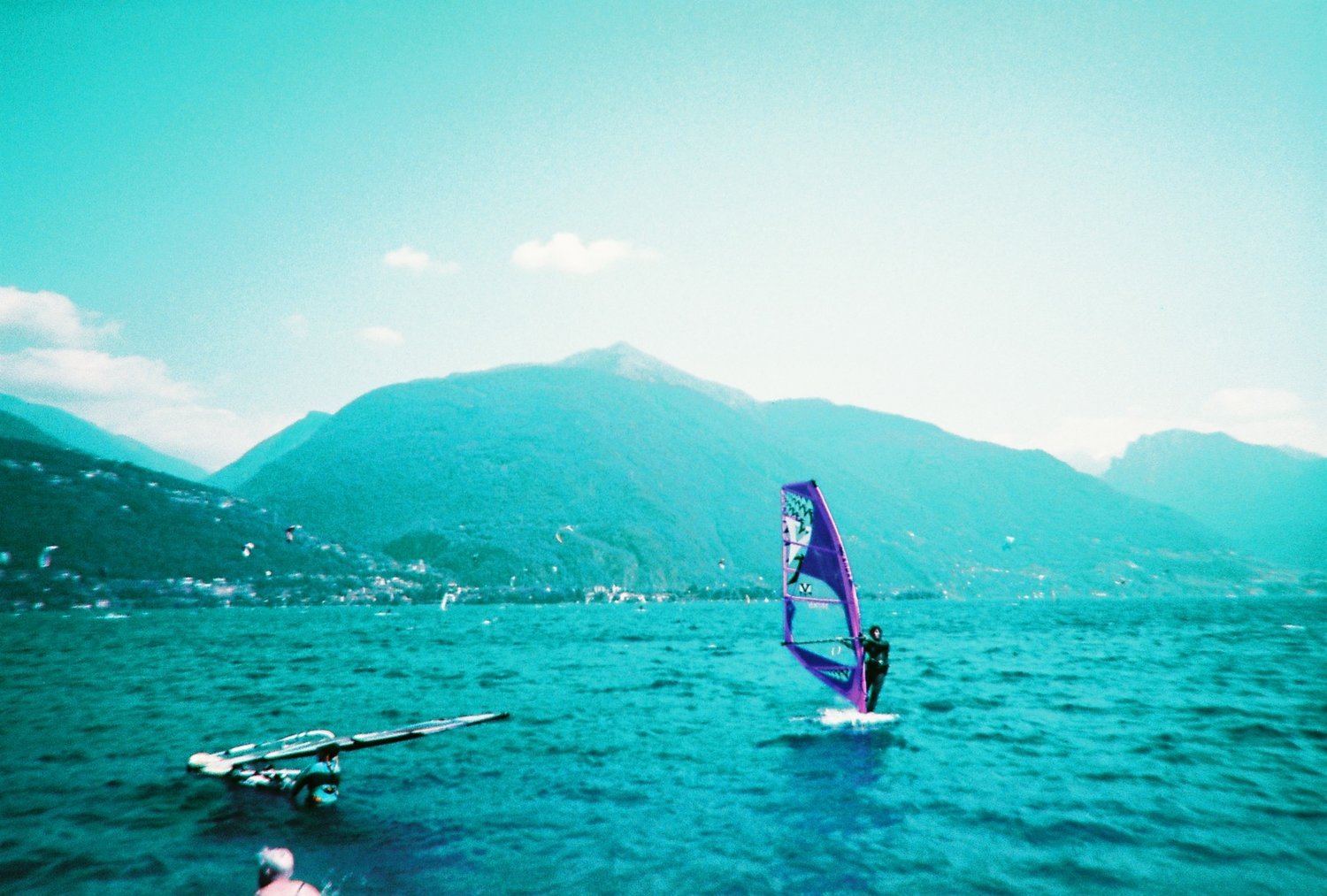 Person windsurfing on a lake with a mountainous backdrop and clear sky.