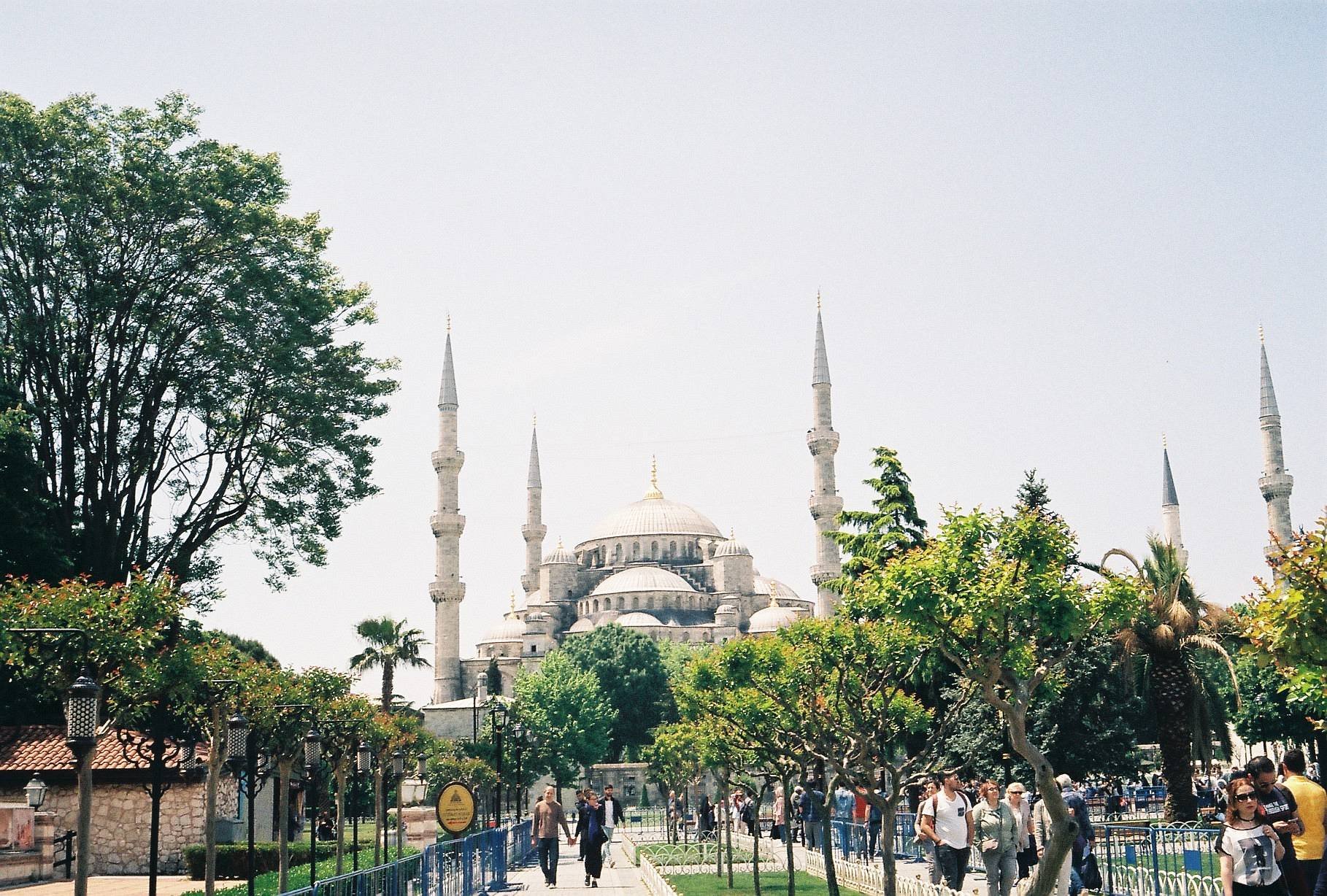 Blue Mosque in Istanbul with minarets, trees, and people walking.