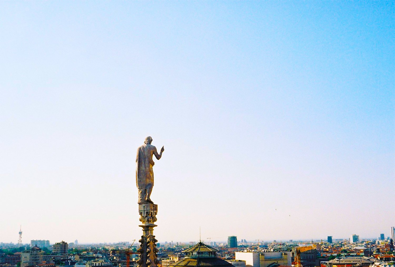Statue on rooftop overlooking a city skyline with clear blue sky.