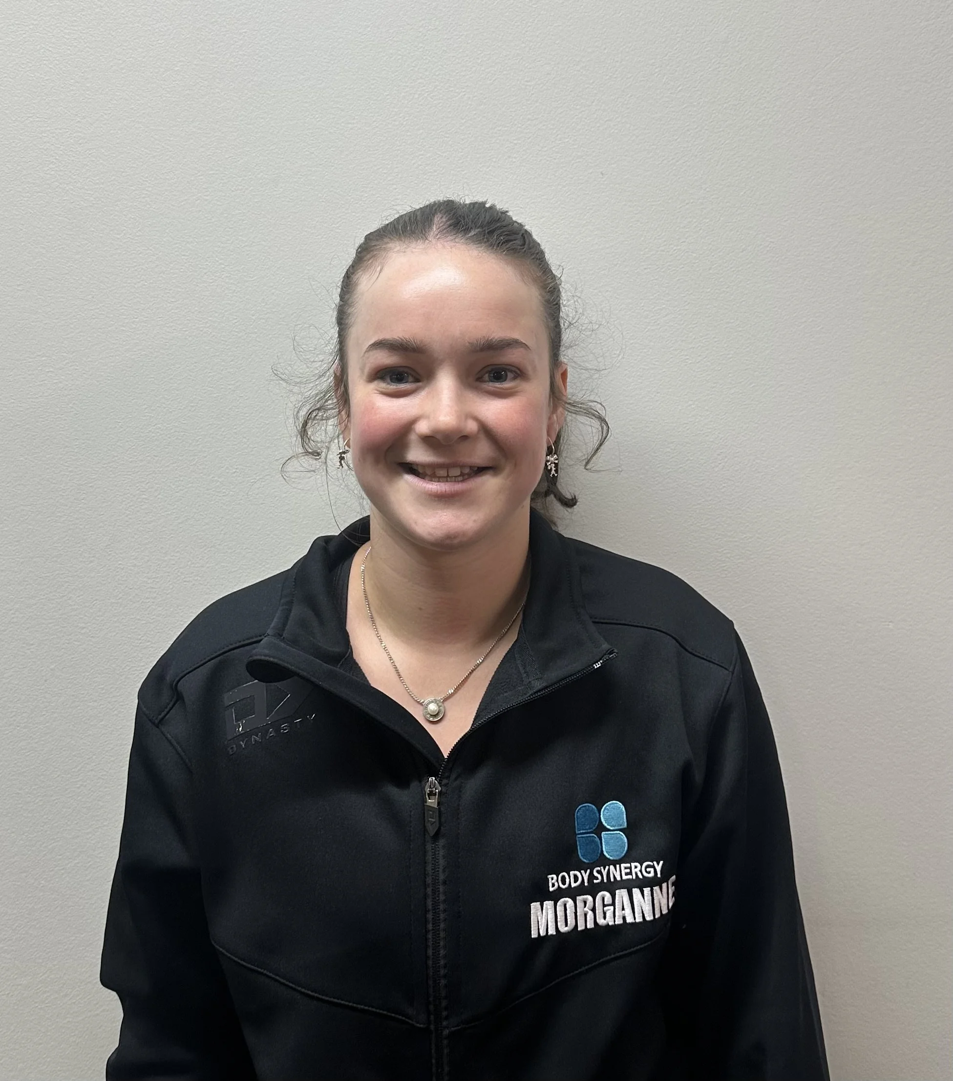 A person smiling, wearing a dark jacket with the logo "Body Synergy" and "Grace" visible on it.