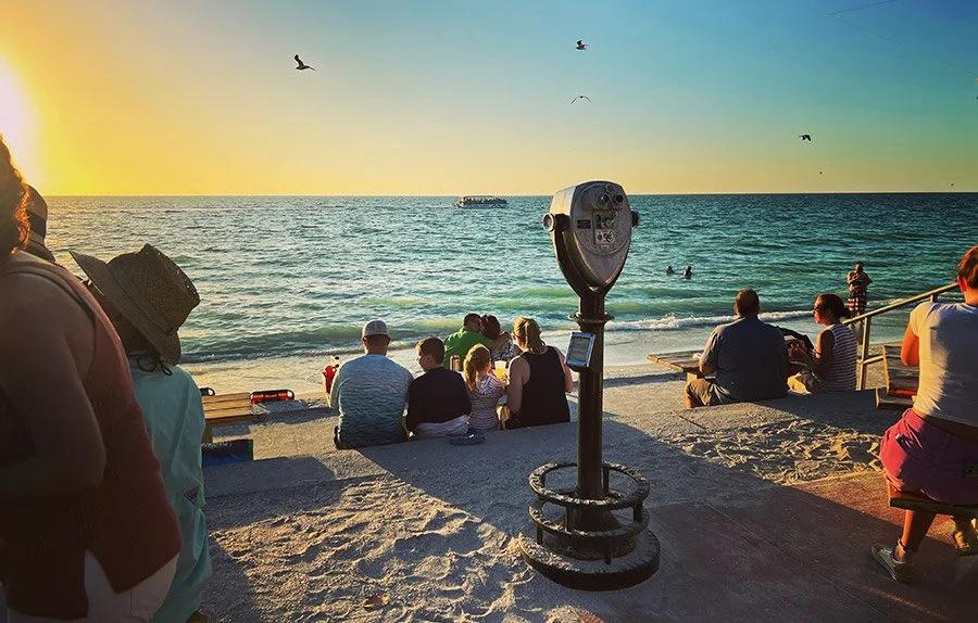 Visitors enjoying sunset views at Pass-a-Grille Beach, Florida, with oceanfront seating, family gatherings, and Gulf Coast charm.
