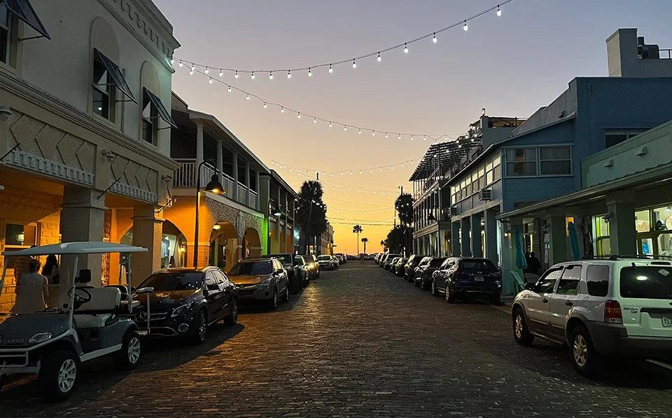 Scenic sunset view of historic 8th Avenue in Pass-a-Grille, Florida, with string lights, boutique shops, and beachside charm.