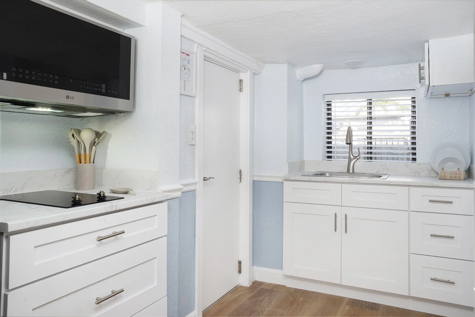 Kitchen with white cabinets, marble countertops, a window with blinds, a sink, a microwave, and a stovetop.