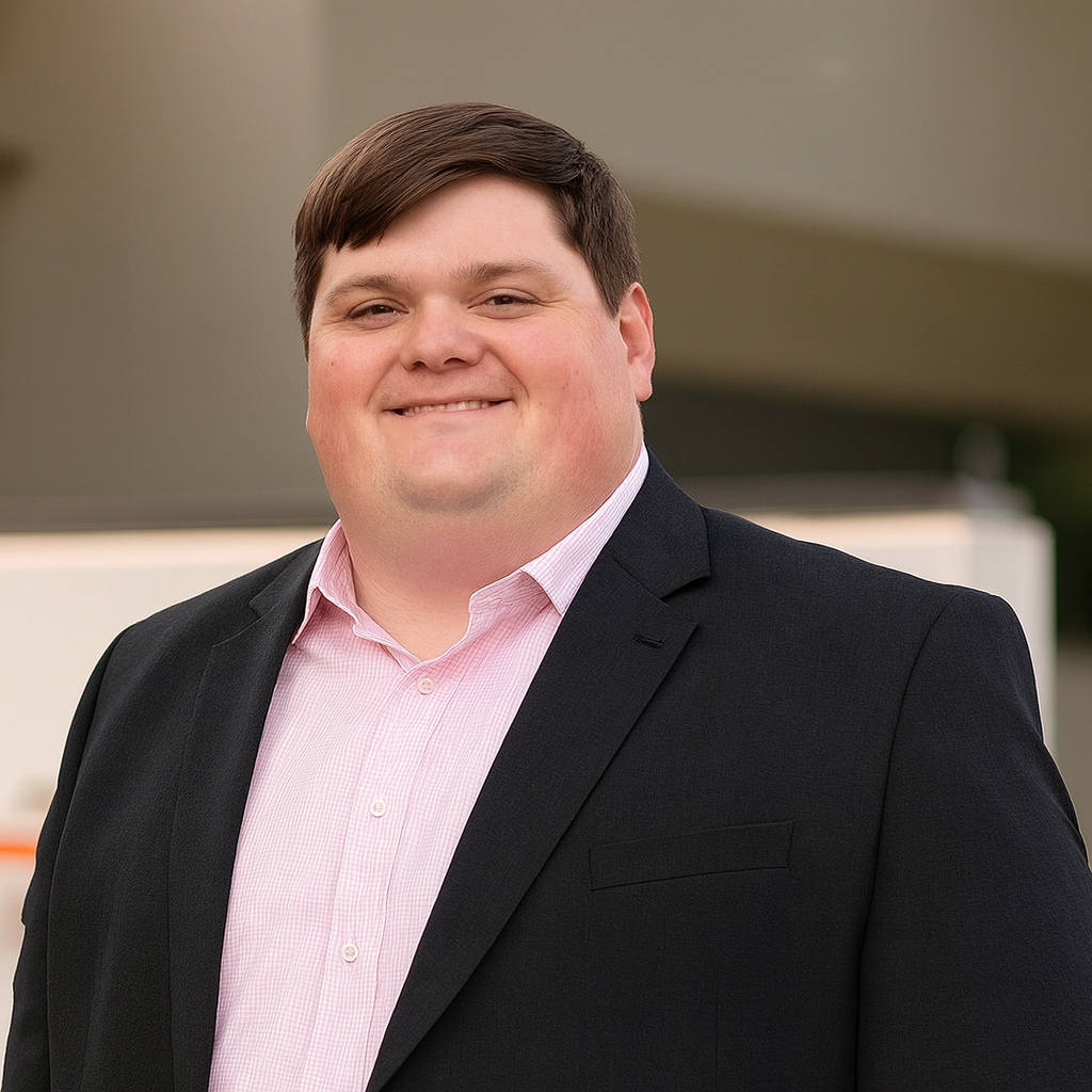 Man in a blue suit and plaid tie smiling against a gray background.