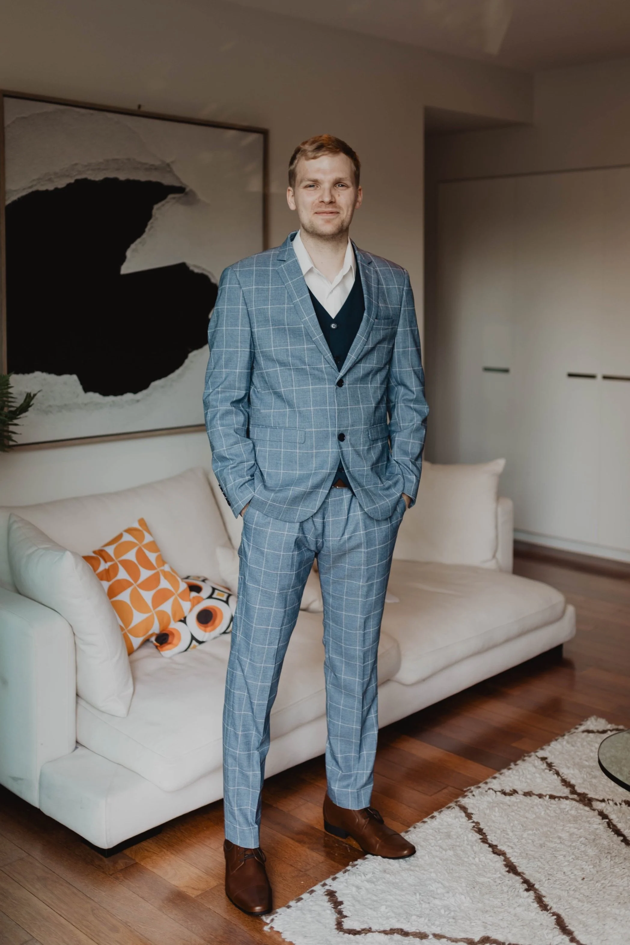 A man in a blue checked suit standing in a living room.