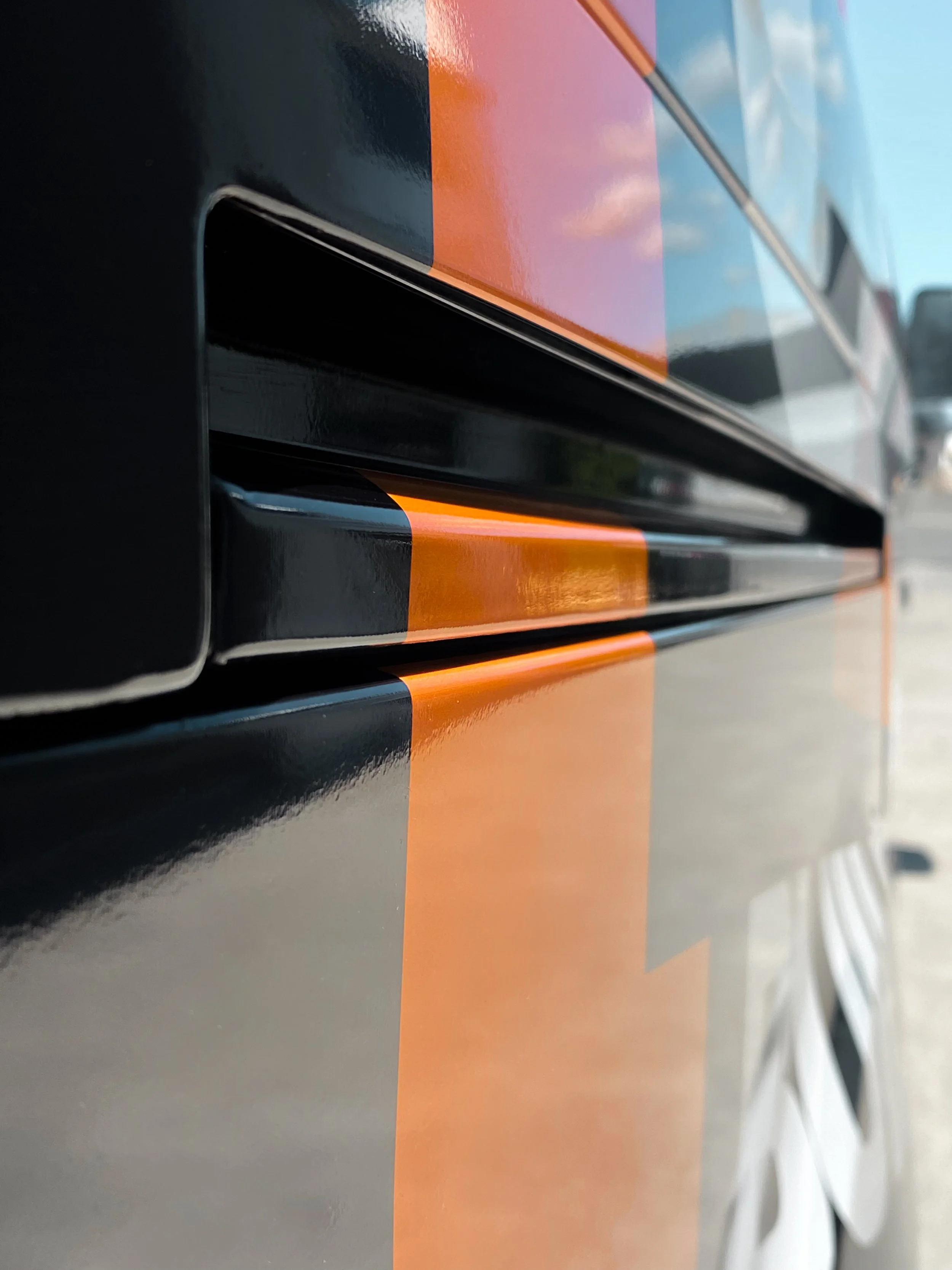 Close-up of a black vehicle with orange and black racing stripe.