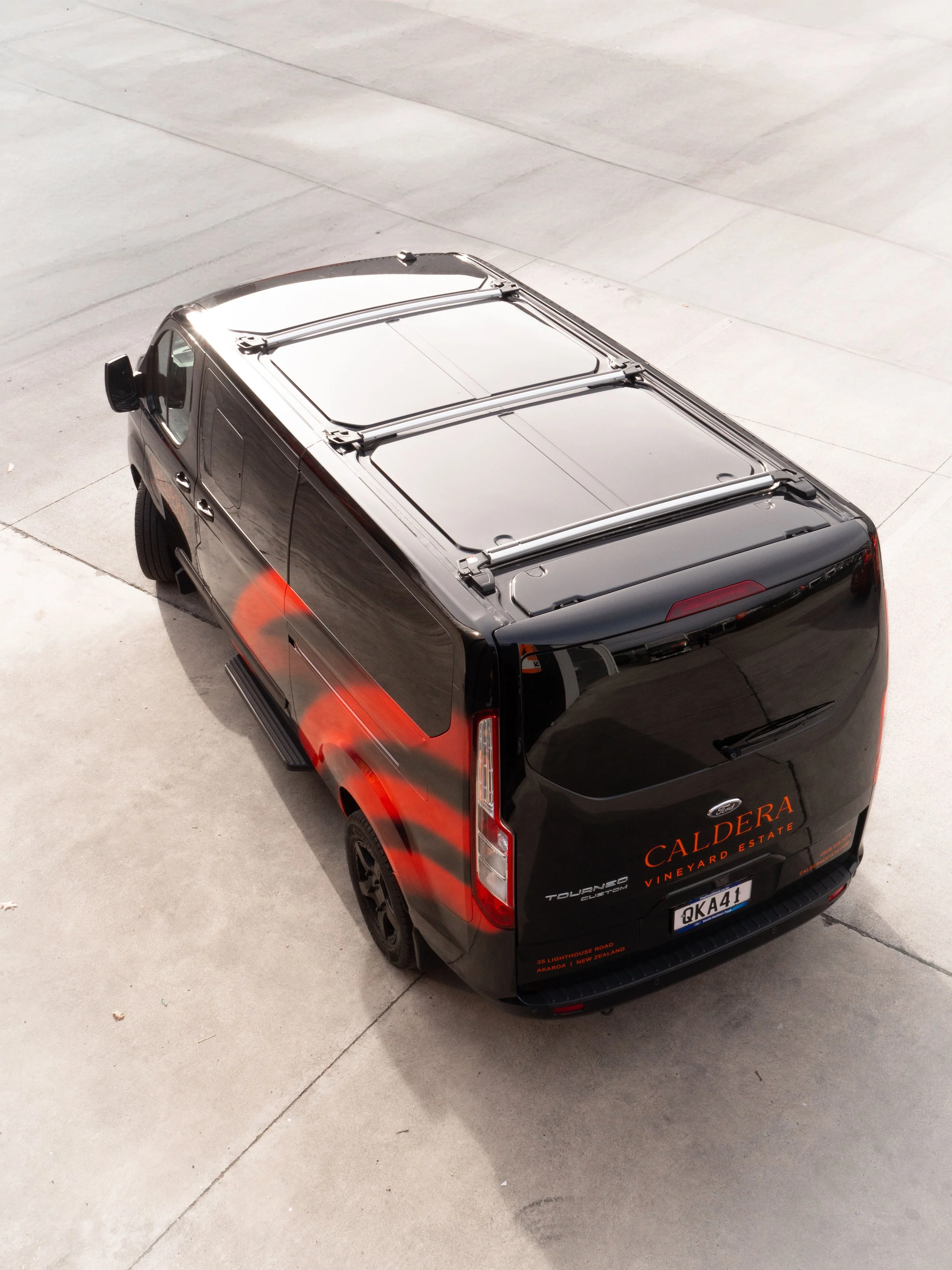 Black van with orange and red graphics and the words 'Caldera Vineyard Estate' parked on a concrete surface, viewed from above and at an angle.