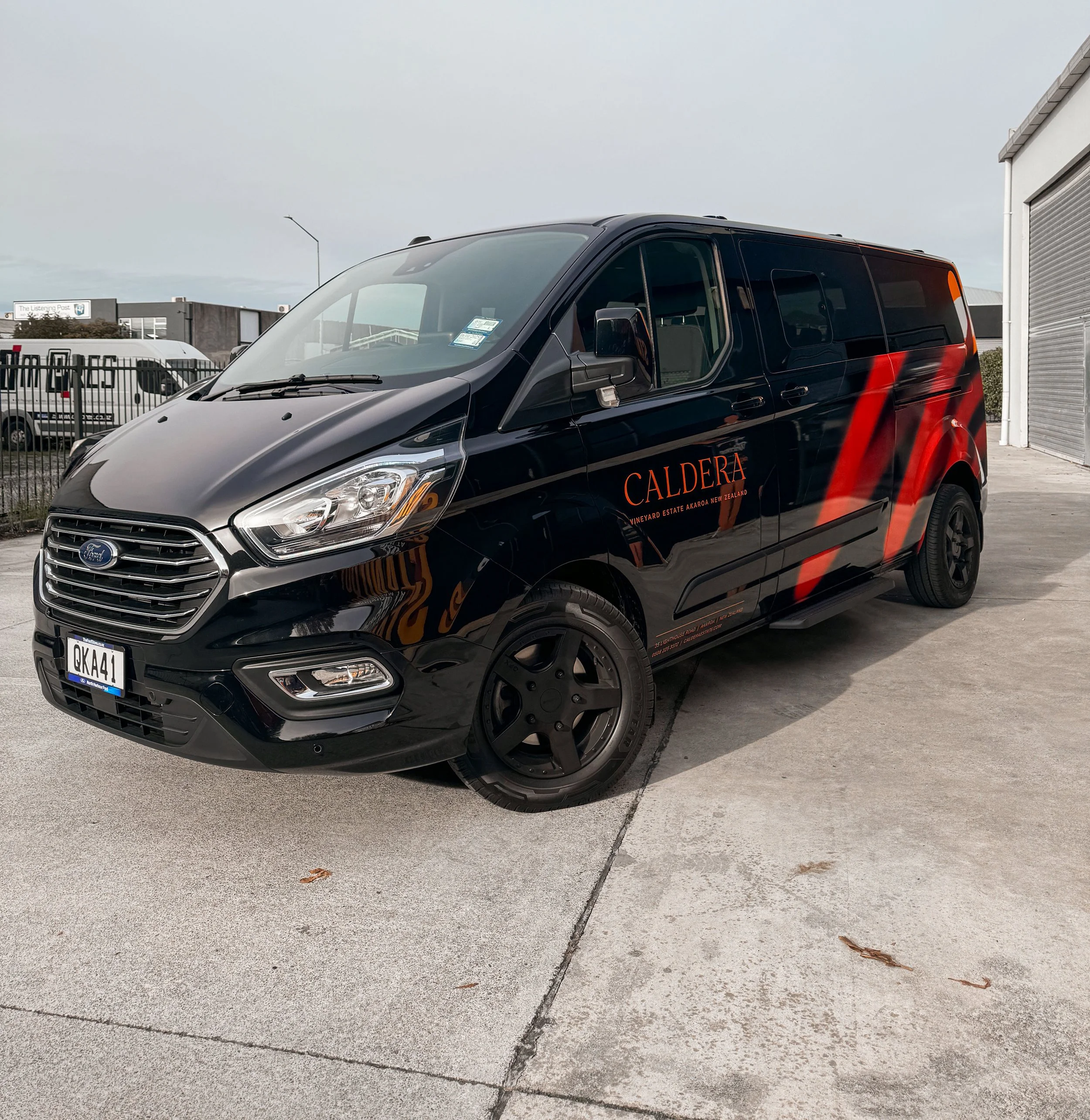 Black van with red and orange branding for Caldera winery, parked on concrete pavement near industrial buildings.