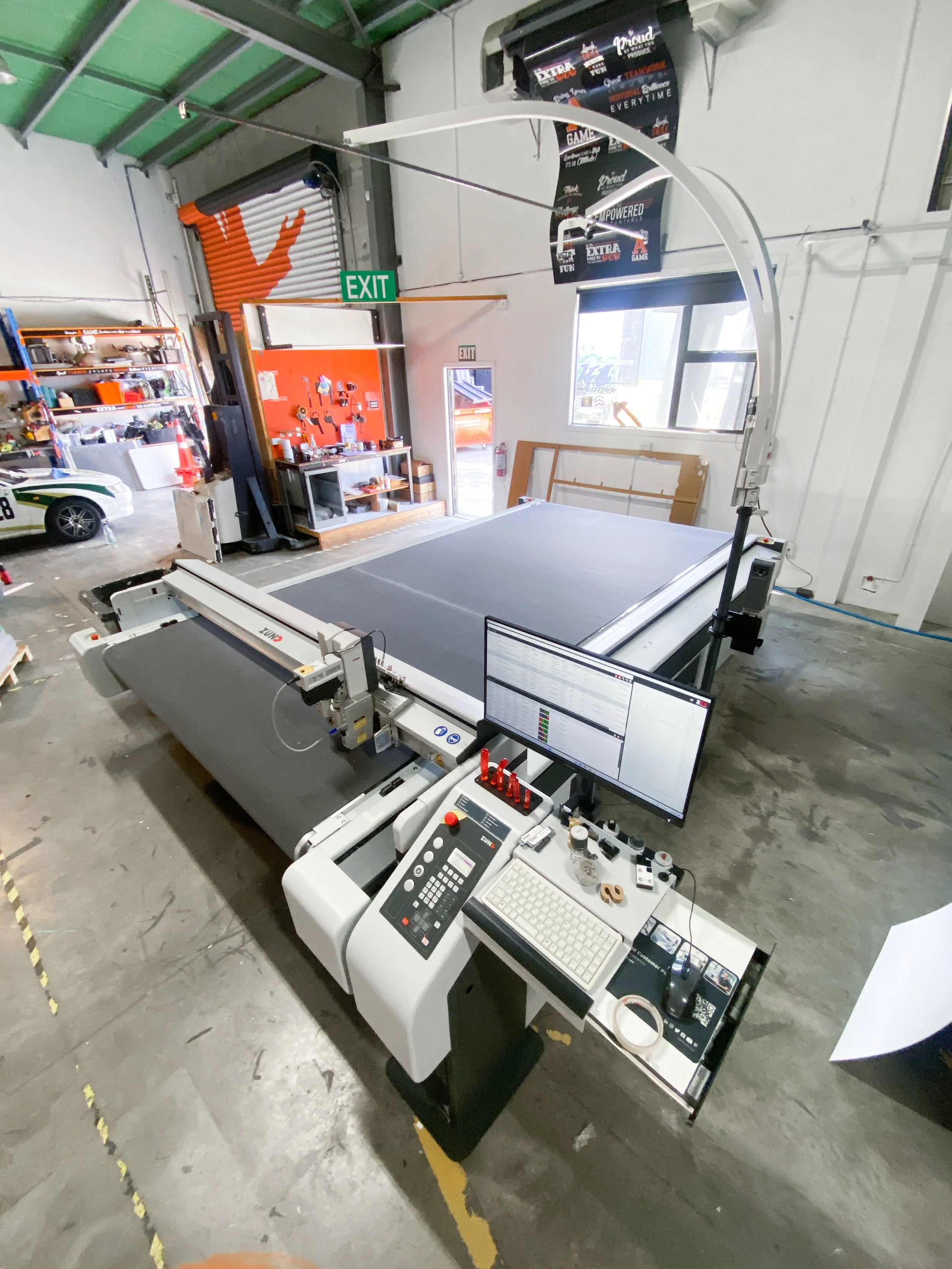 Large industrial CNC laser cutting machine with computer monitor, keyboard, and control panel in a workshop.