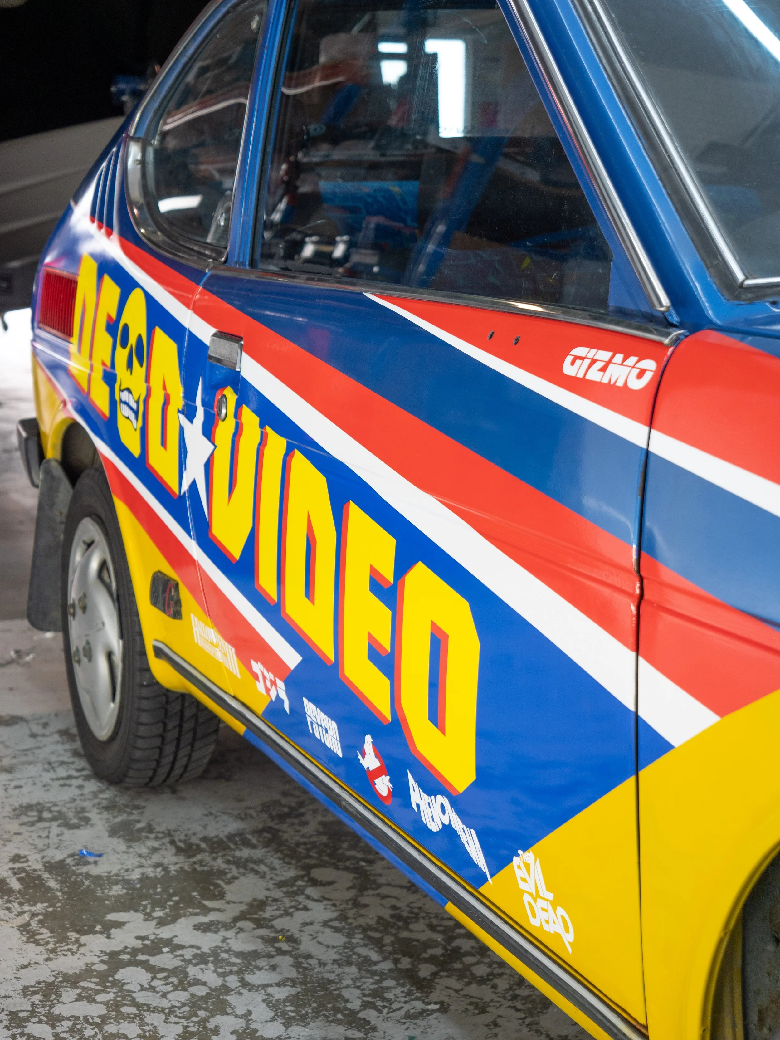 Car with bright, colorful graphics and text that reads 'DELO YUED' in large yellow and blue letters, with various logos and sponsors.