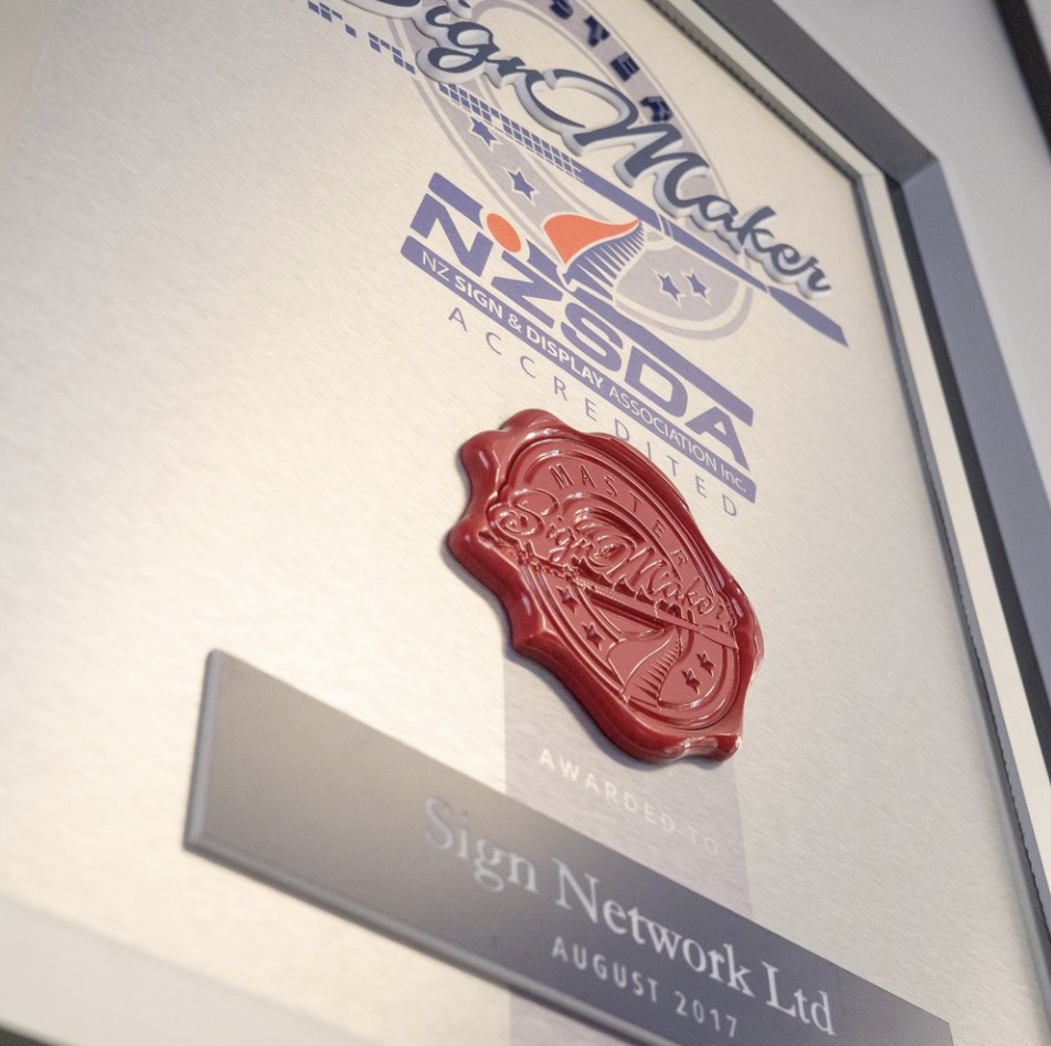 A framed award certificate from NZ Sign & Display Association Inc., dated August 2017, with a red wax seal and stylized American flag logo at the top. The certificate recognizes Sign Network Ltd.