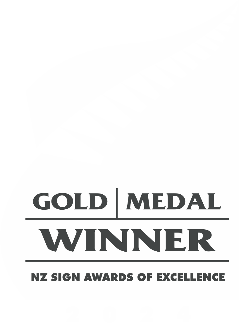 A black and white vertical badge design for the NZ Sign Awards of Excellence in 2024, with a stylized wavy flag and a row of black rectangles resembling a banner text area, featuring the text 'Gold Medal Winner' and 'NZ Sign Awards of Excellence'.