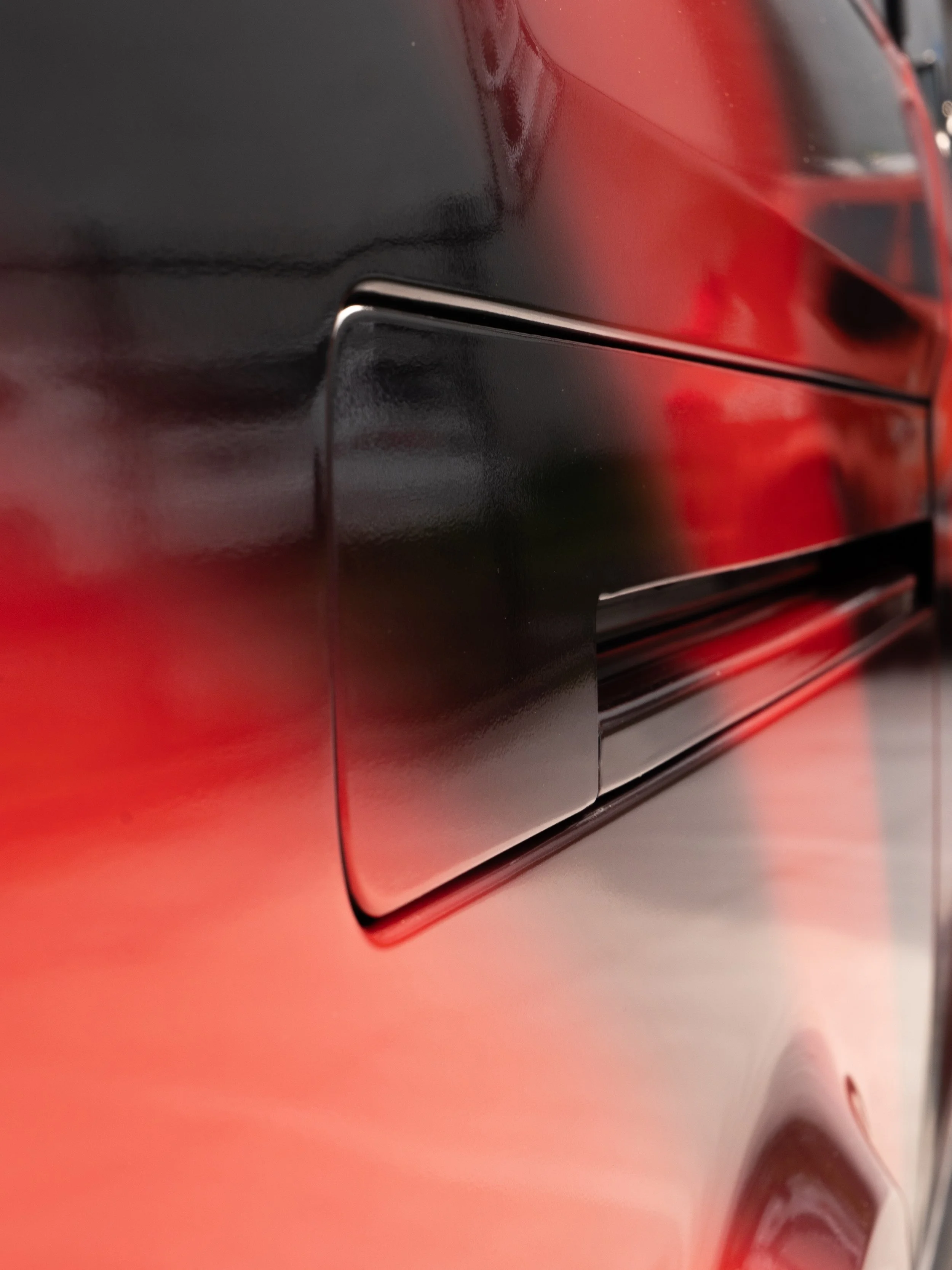 Close-up of a black and red appliance, possibly a dishwasher or oven, showing a sleek handle and surface reflection.