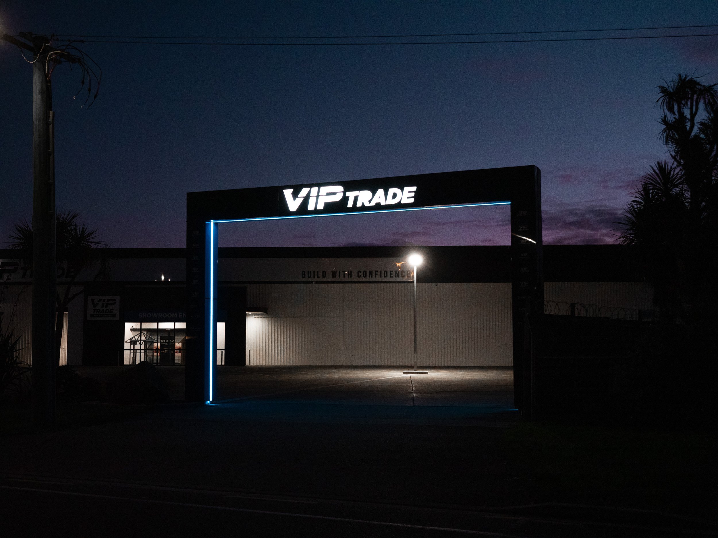 Nighttime view of the VIP Trade building entrance with illuminated sign and archway, with nearby trees and a bright streetlamp.