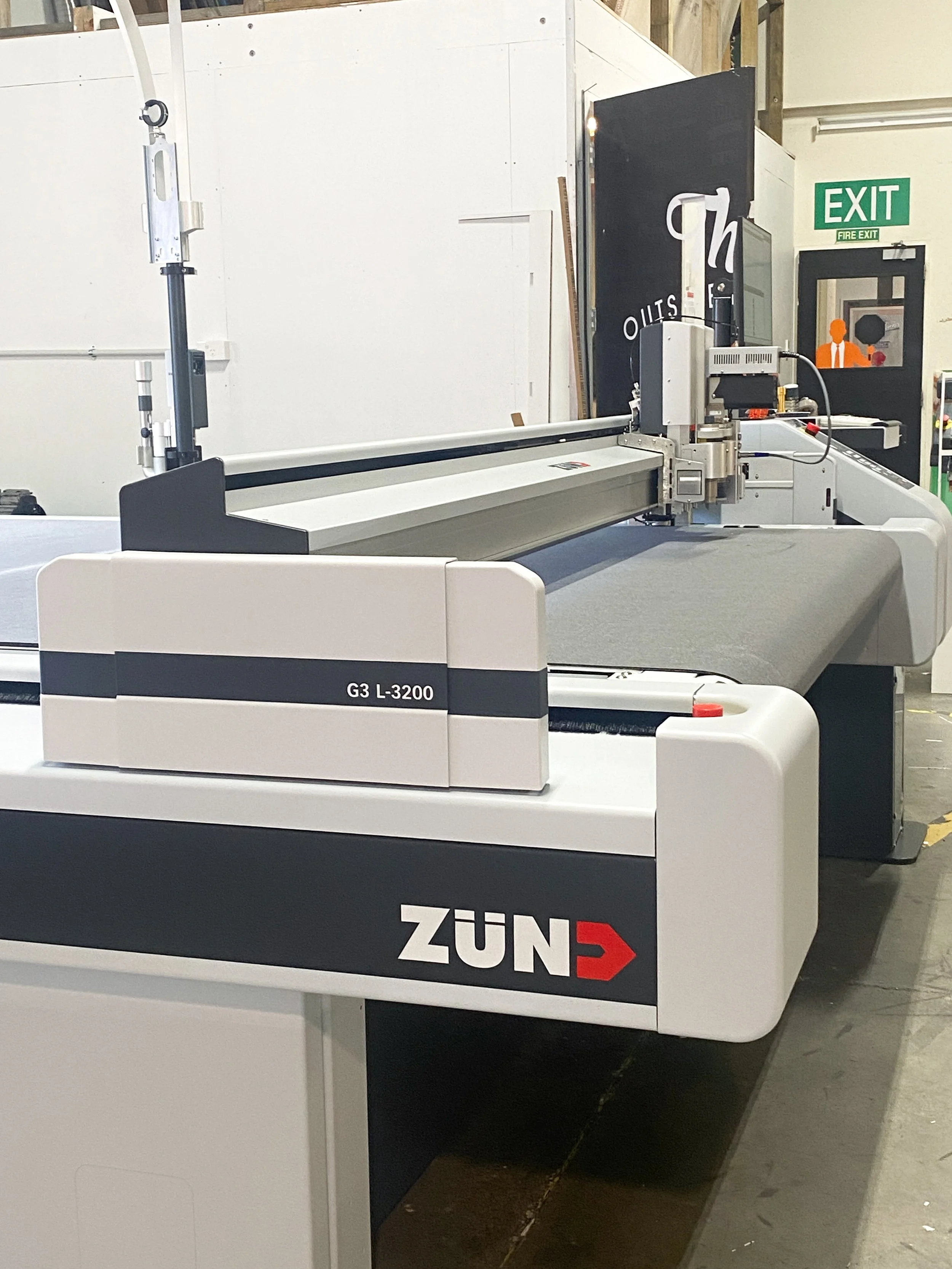 Large industrial Zünd digital cutting machine in a workspace, with a gray cutting surface and electronic components.