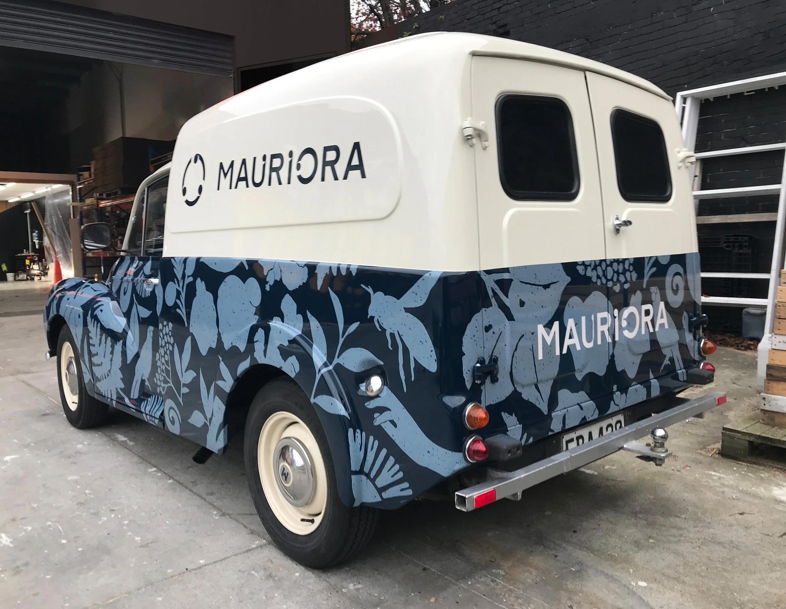 Vintage delivery van with a blue floral and insect pattern on the lower half and white upper half, displaying the word 'MAURÏORA' on the side and back.