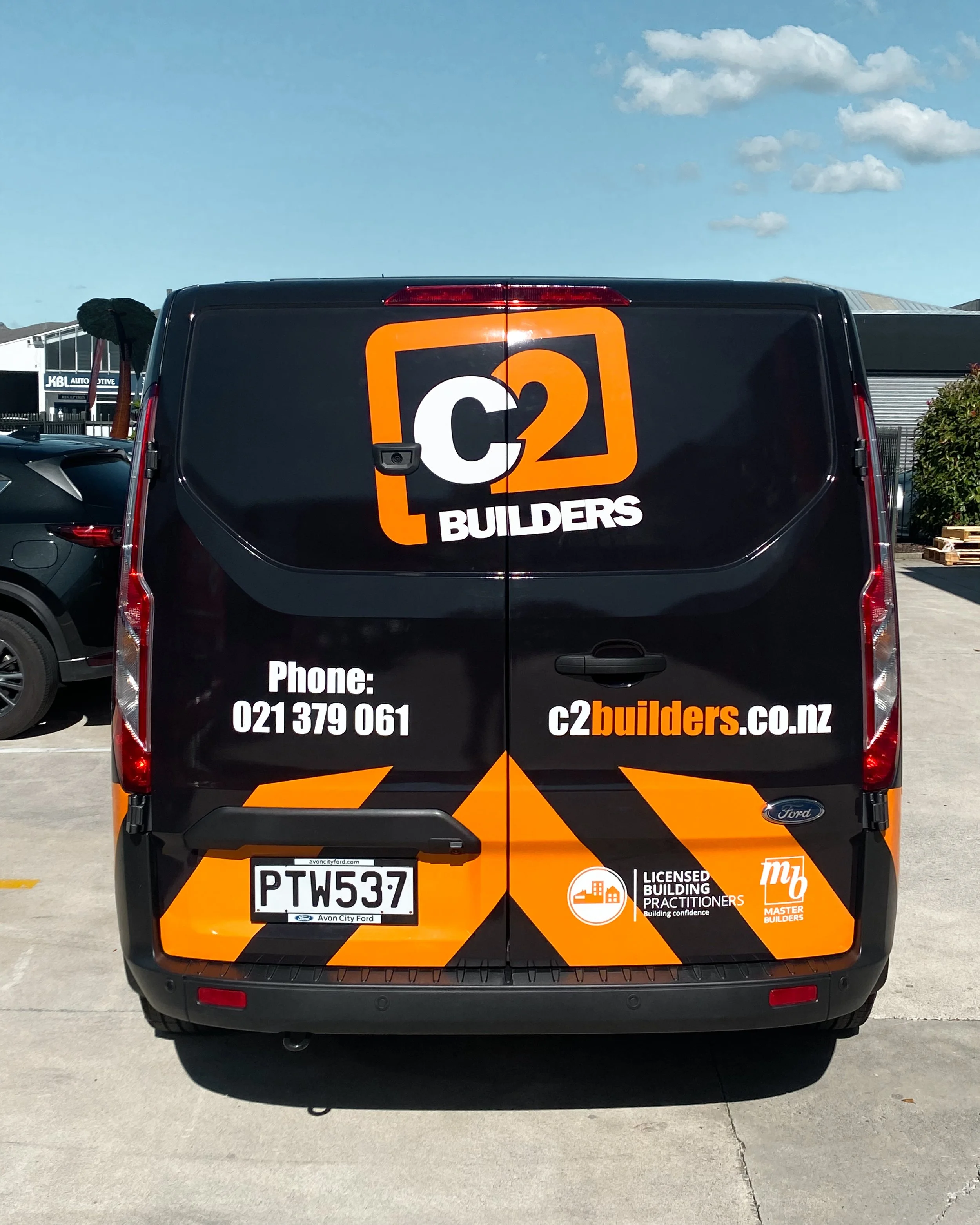 Back of a black van with C2 Builders branding, contact number, website, a licensed building practitioner logo, and a Master Builders logo.