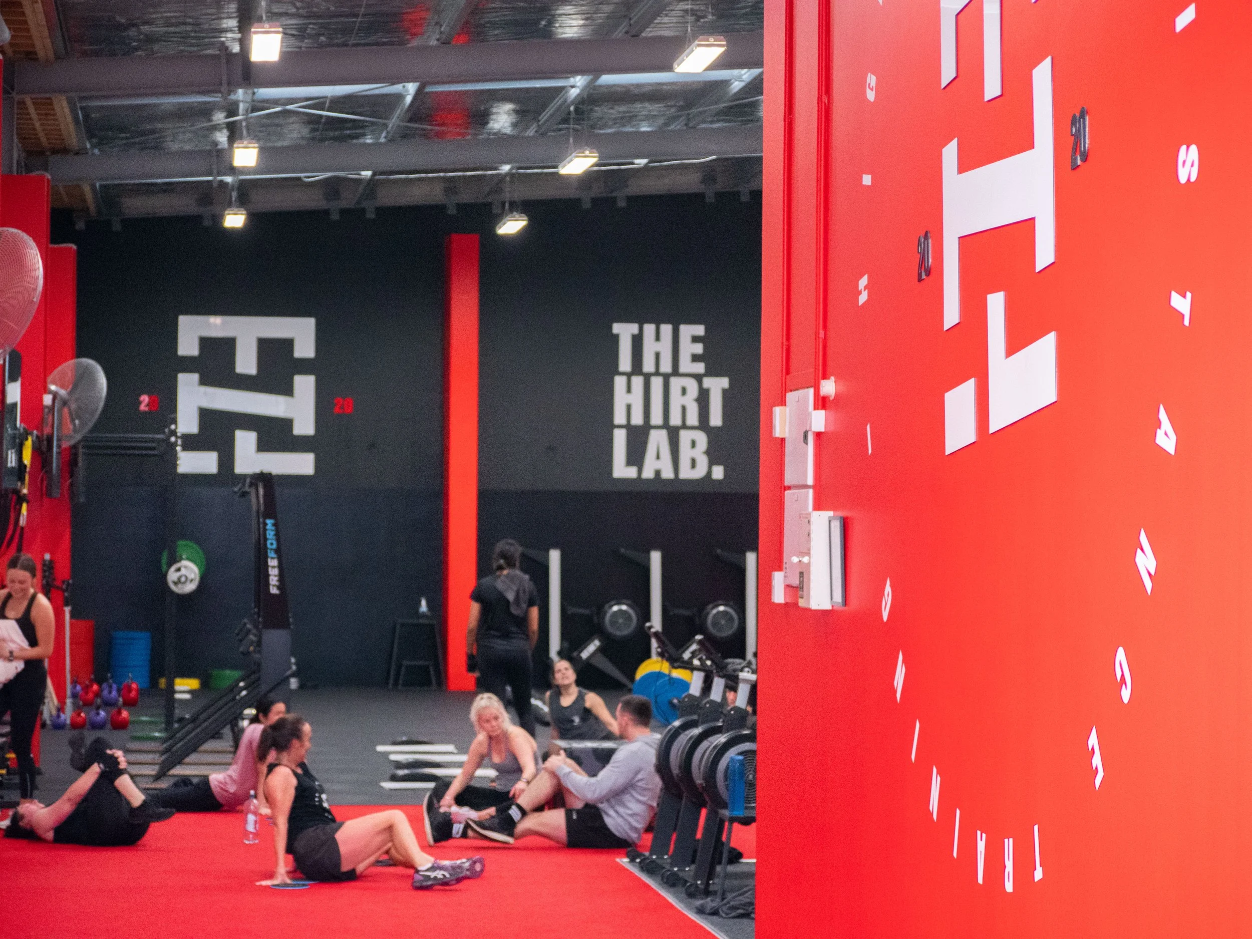 People resting and stretching in a fitness gym with black and red walls displaying words and numbers
