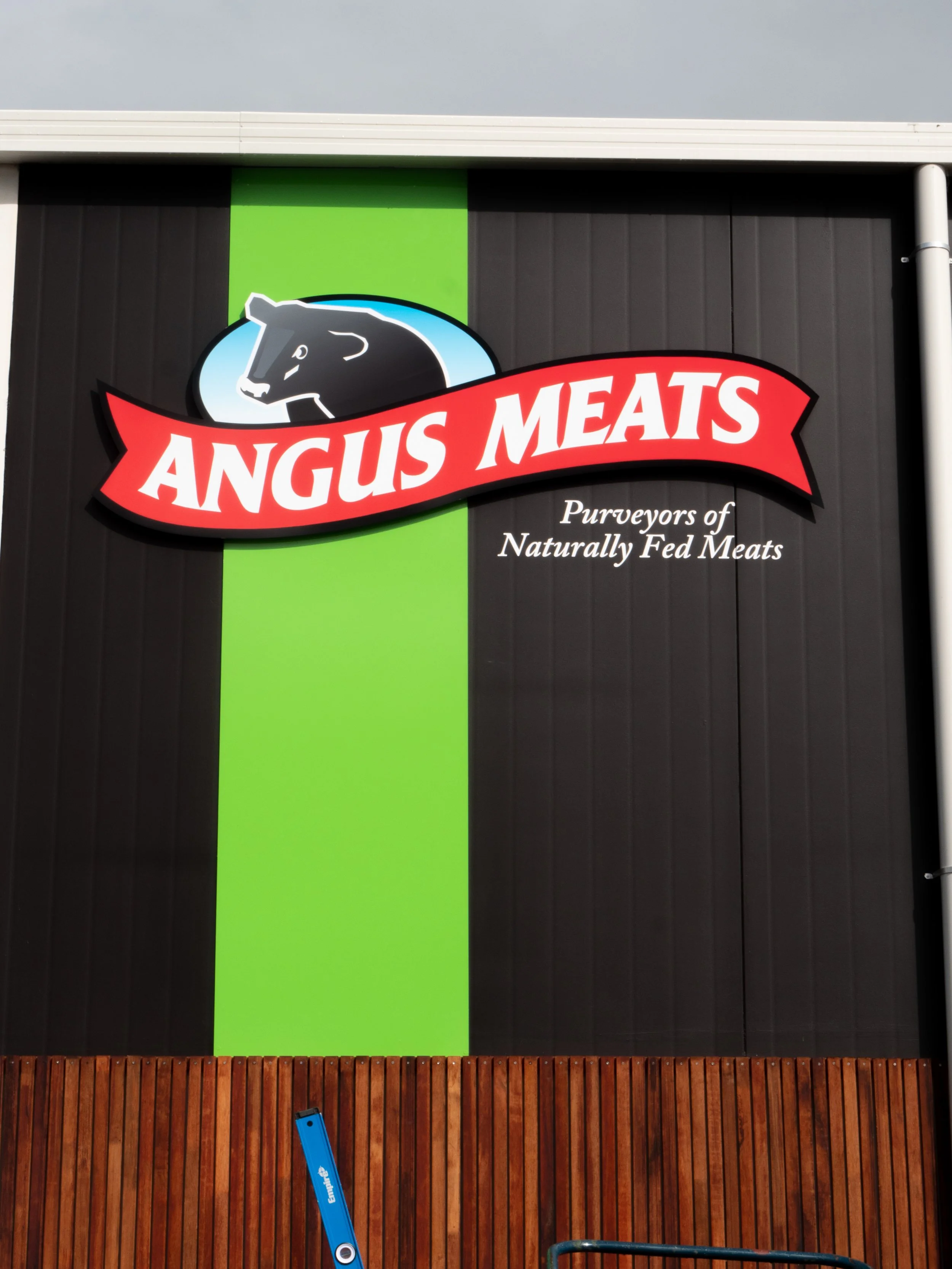 Signboard for Angus Meats with a logo of a black bear's head inside a blue oval and the slogan "Purveyors of Naturally Fed Meats" below.