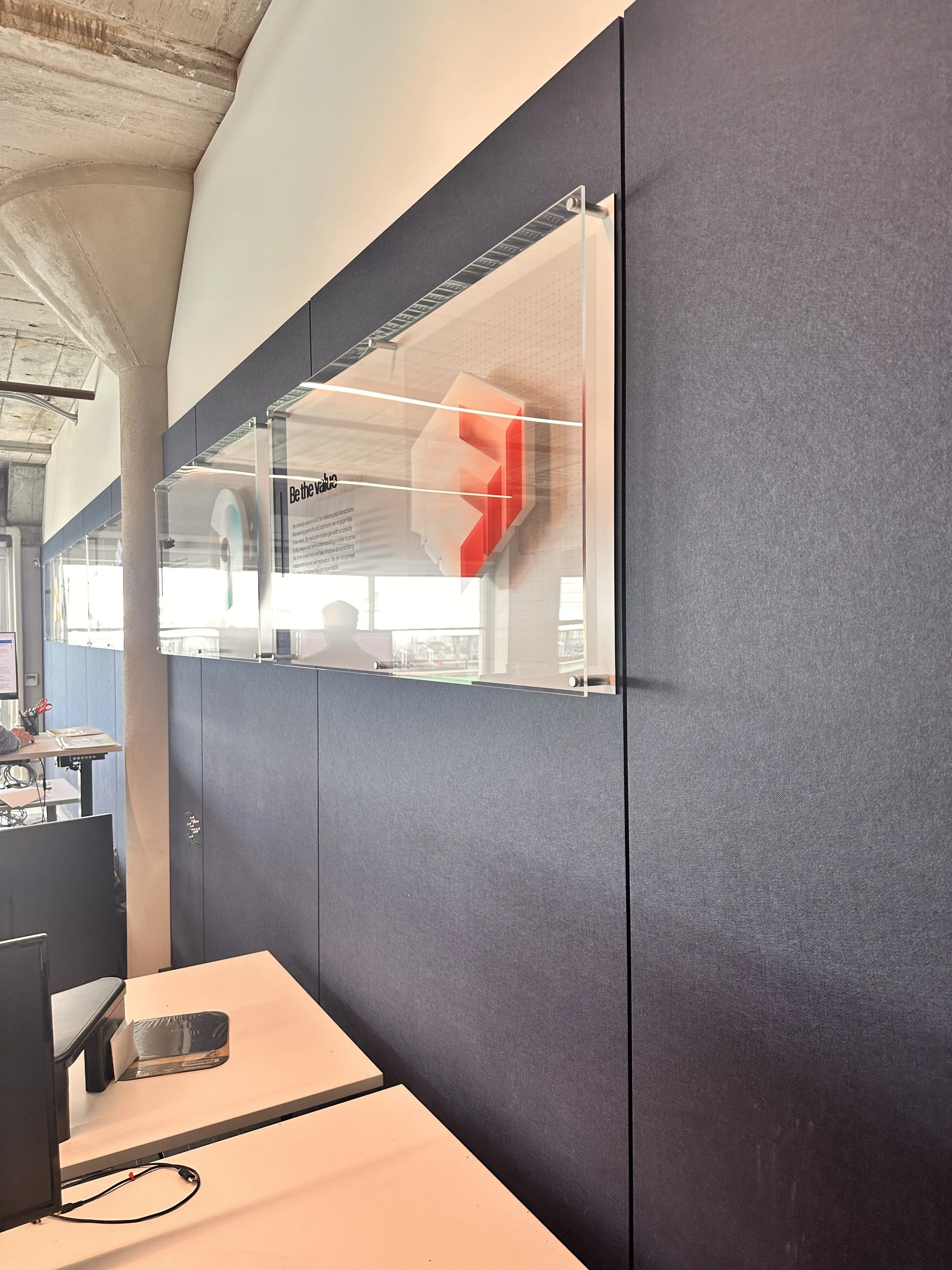 Interior view of an office with a dark gray partition wall and a clear display case with an illuminated red arrow and informational text.