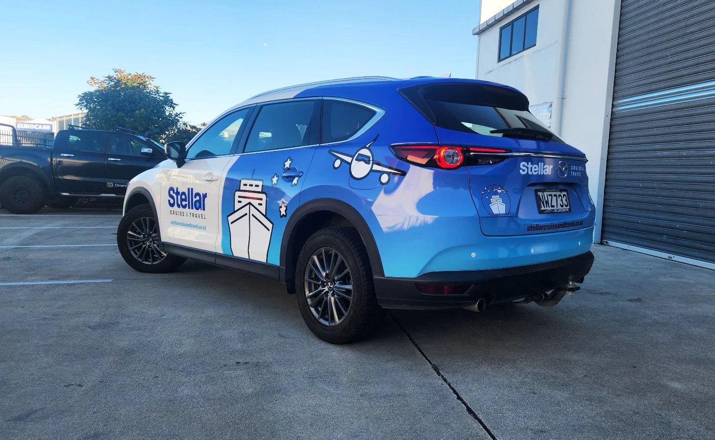 Blue and white leasing or company vehicle with space-themed graphics, including a spaceship, stars, and planets, parked outdoors near a building with a garage door.