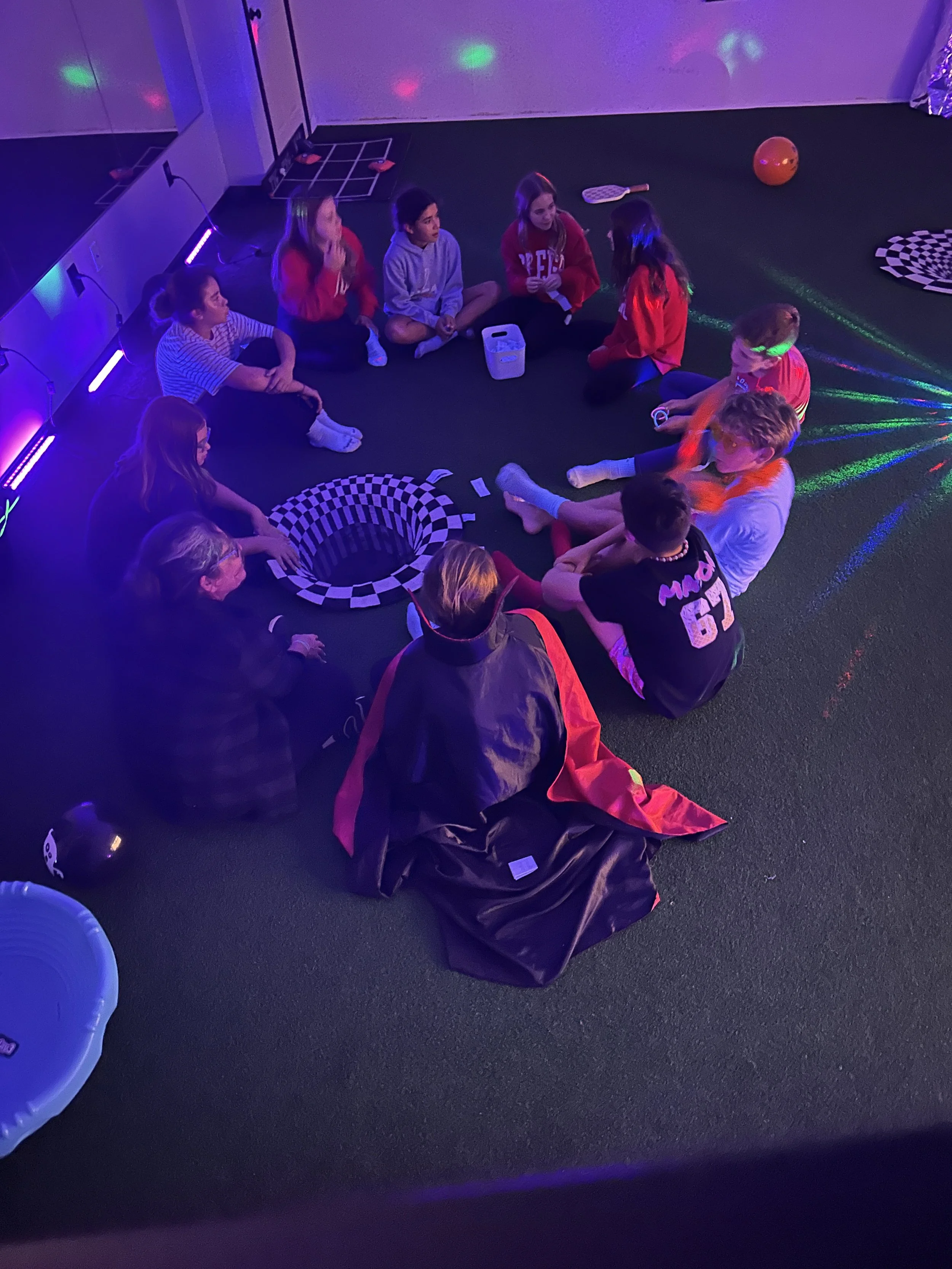 Kids sitting together in a circle playing Halloween charades at The Clubhouse Wellness Center — encouraging social-emotional learning, laughter, and peer connection through play.