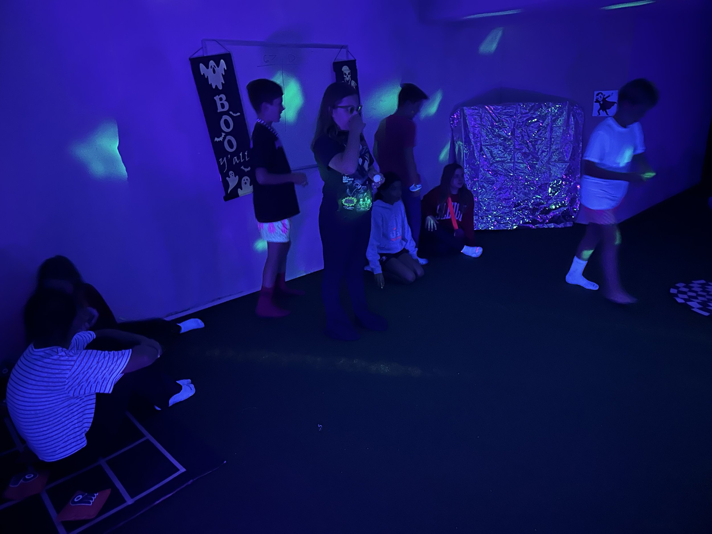 Tween group dancing and playing under colorful lights on The Clubhouse indoor turf Pitch — active, supervised Halloween fun that builds confidence and community.
