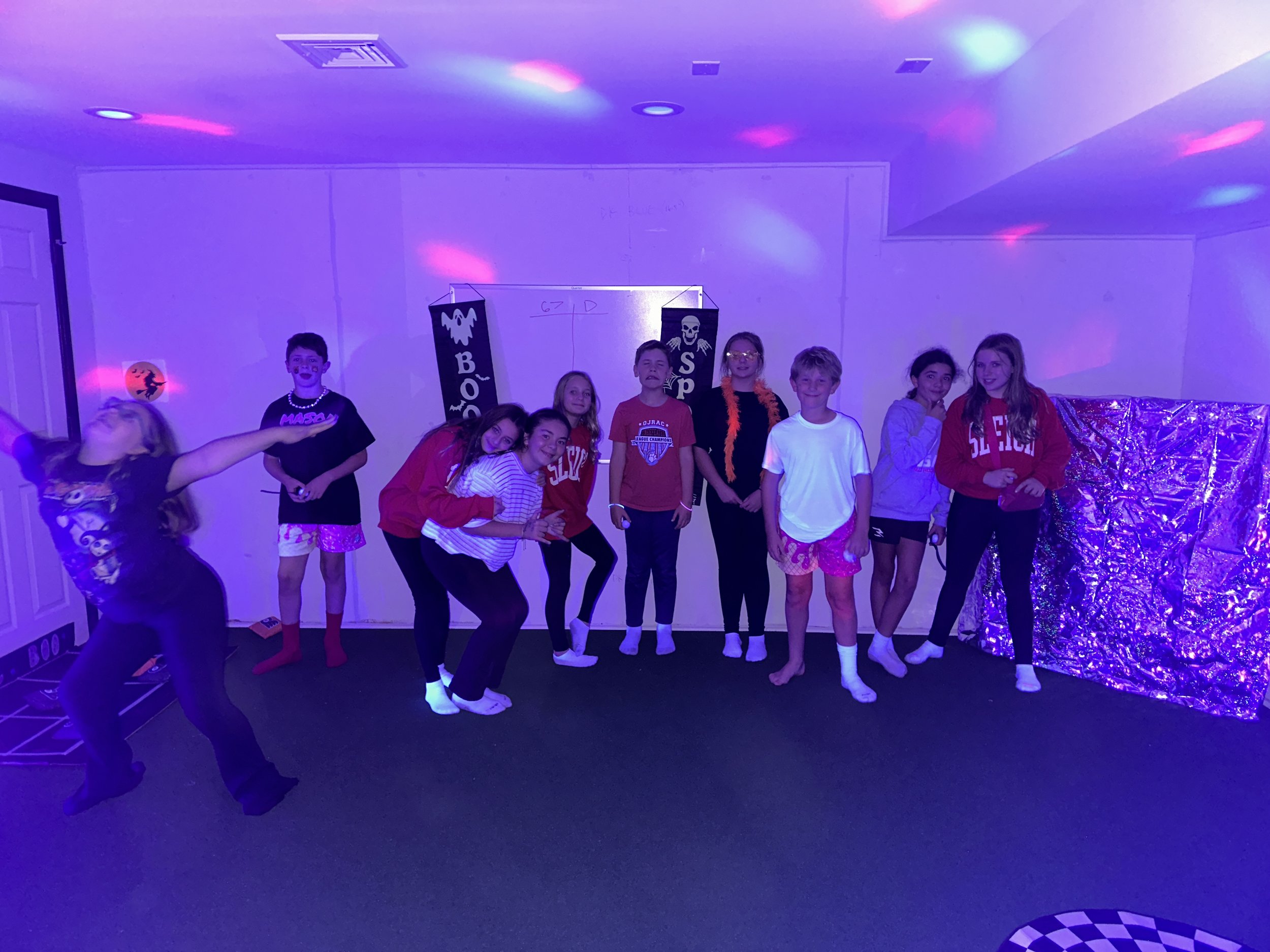 Tween group dancing and playing under colorful lights on The Clubhouse indoor turf Pitch — active, supervised Halloween fun that builds confidence and community.