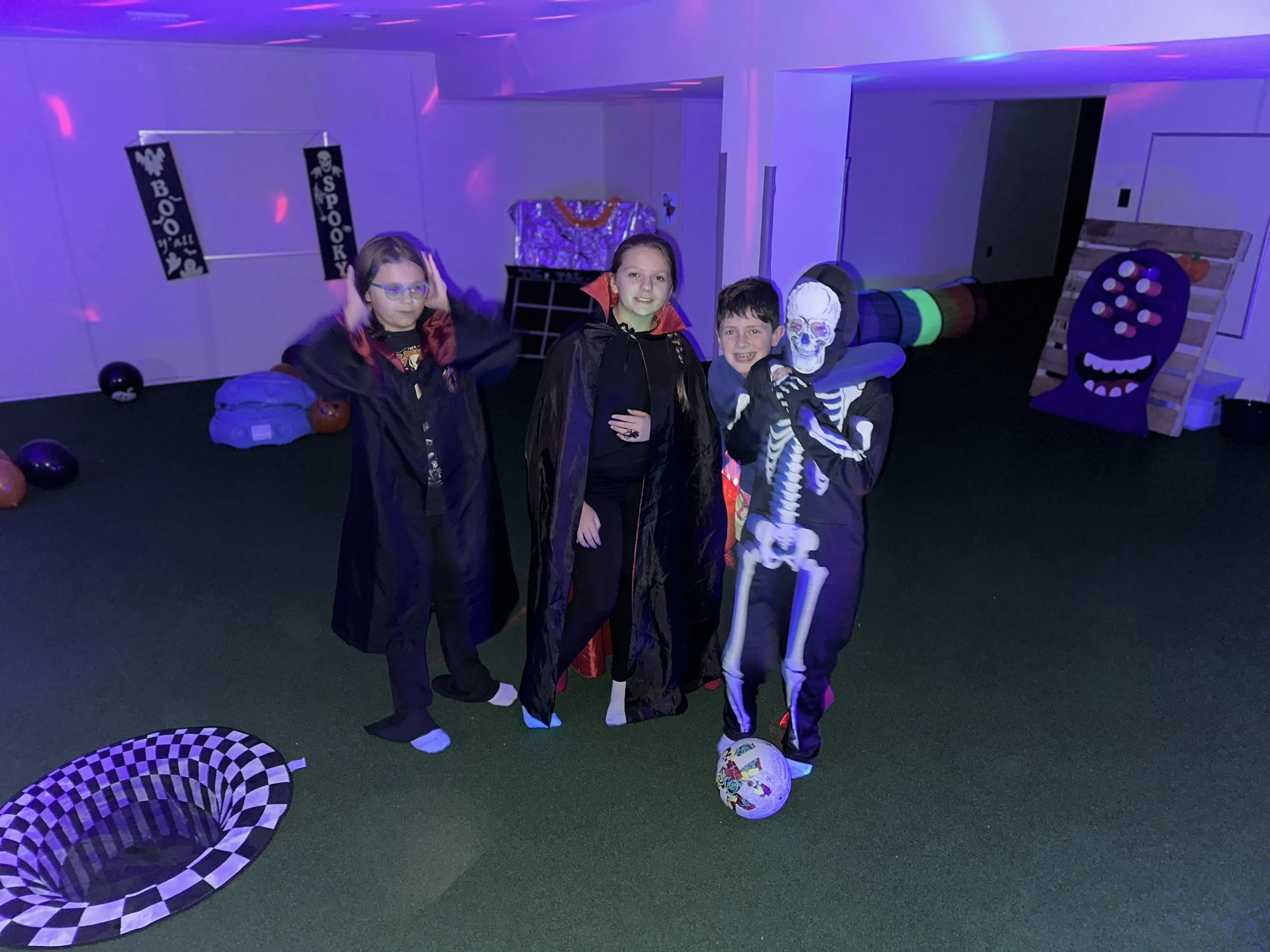 Tween group dancing and playing under colorful lights on The Clubhouse indoor turf Pitch — active, supervised Halloween fun that builds confidence and community.