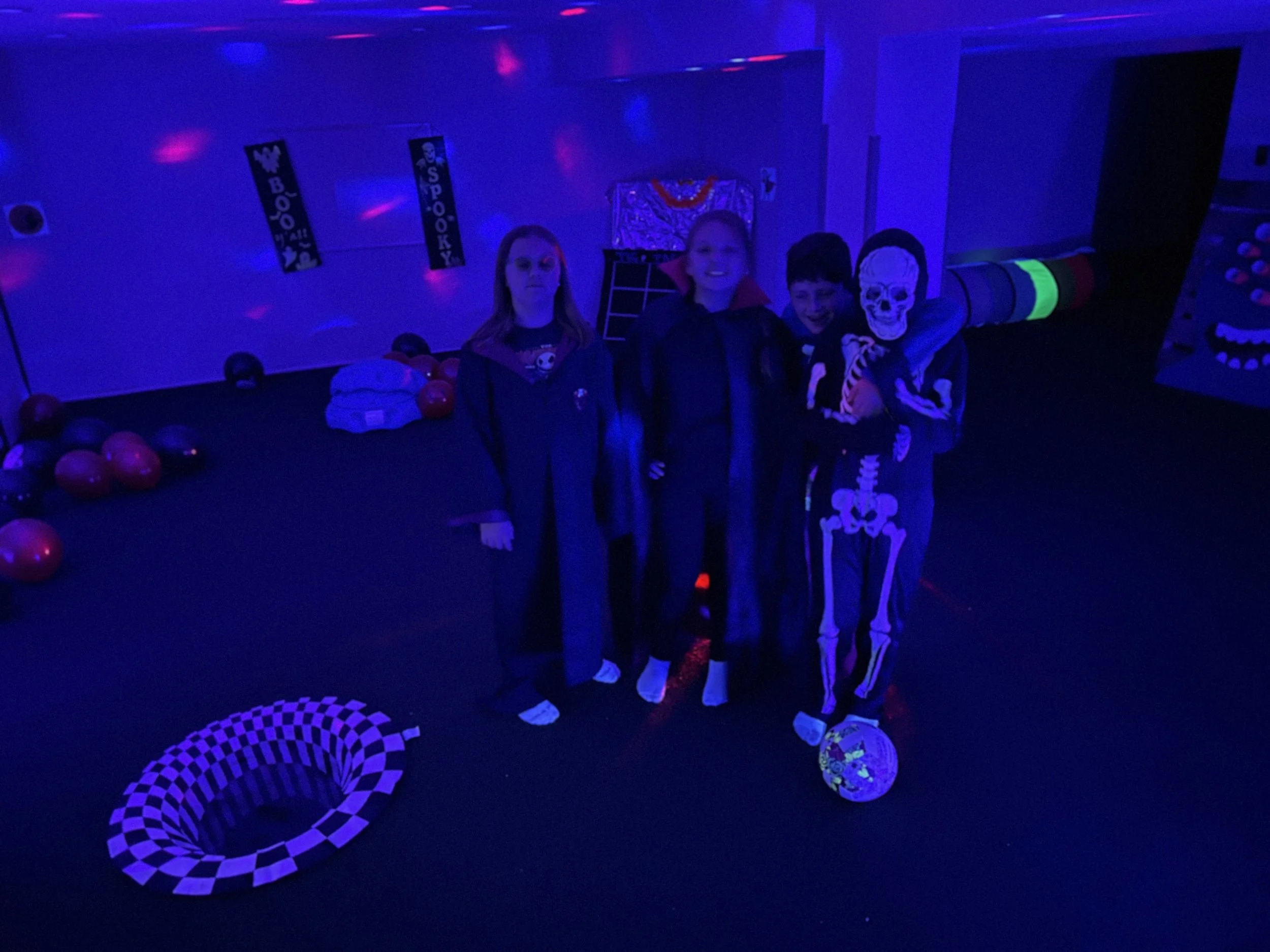Tween group dancing and playing under colorful lights on The Clubhouse indoor turf Pitch — active, supervised Halloween fun that builds confidence and community.