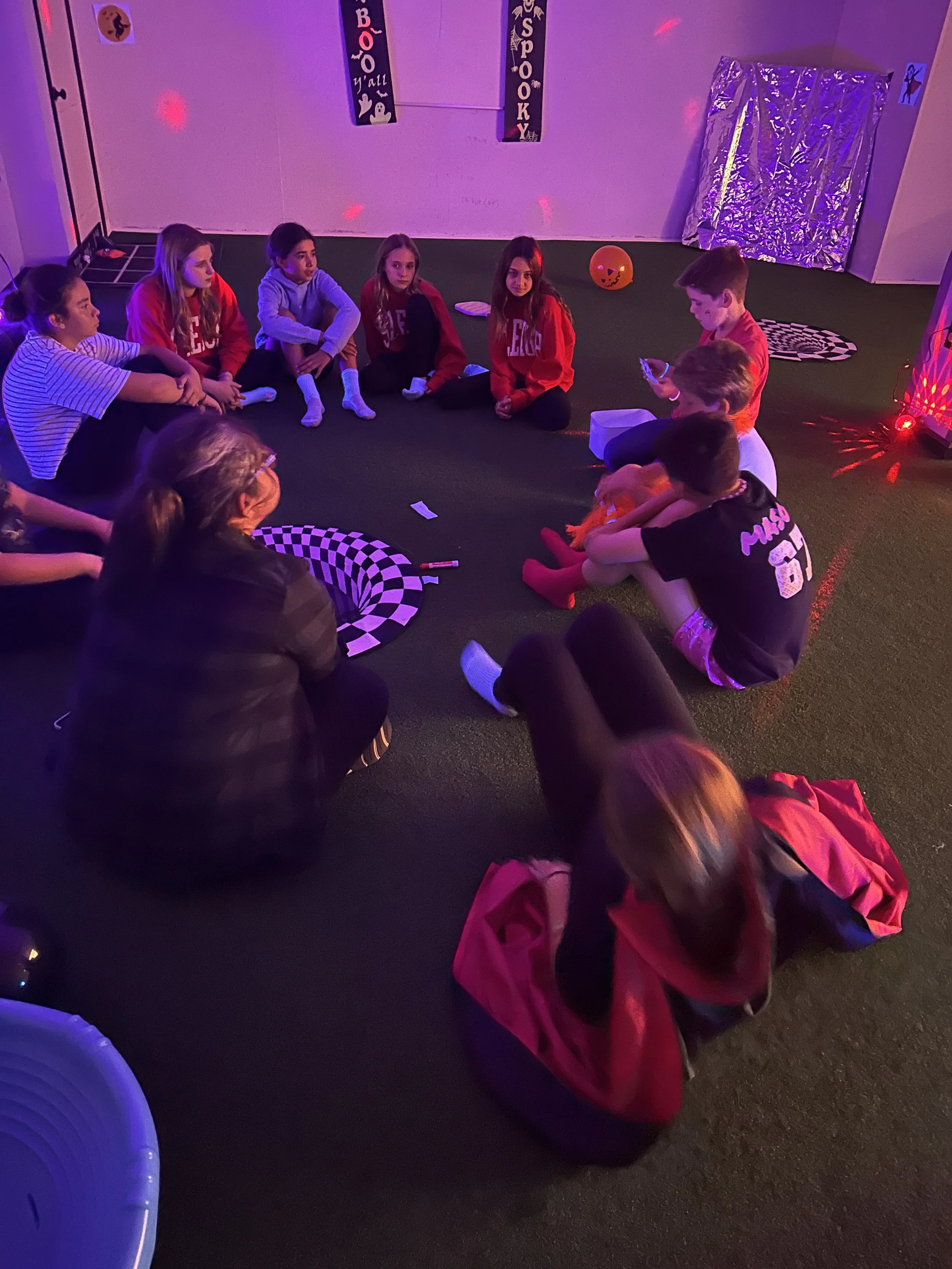 Kids sitting together in a circle playing Halloween charades at The Clubhouse Wellness Center — encouraging social-emotional learning, laughter, and peer connection through play.