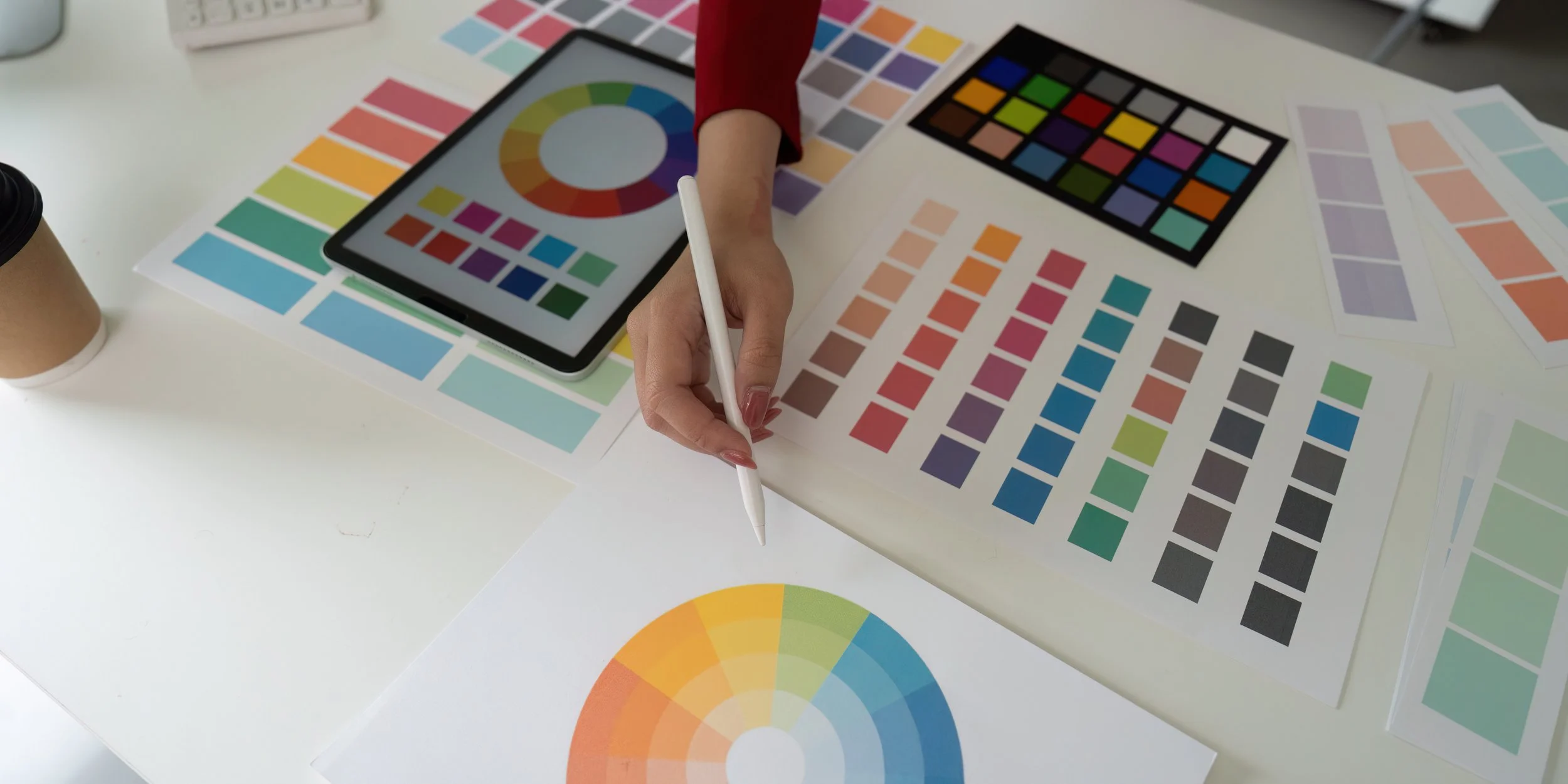 Designer making brand color palette selection. Color charts and wheels laid out across desk.