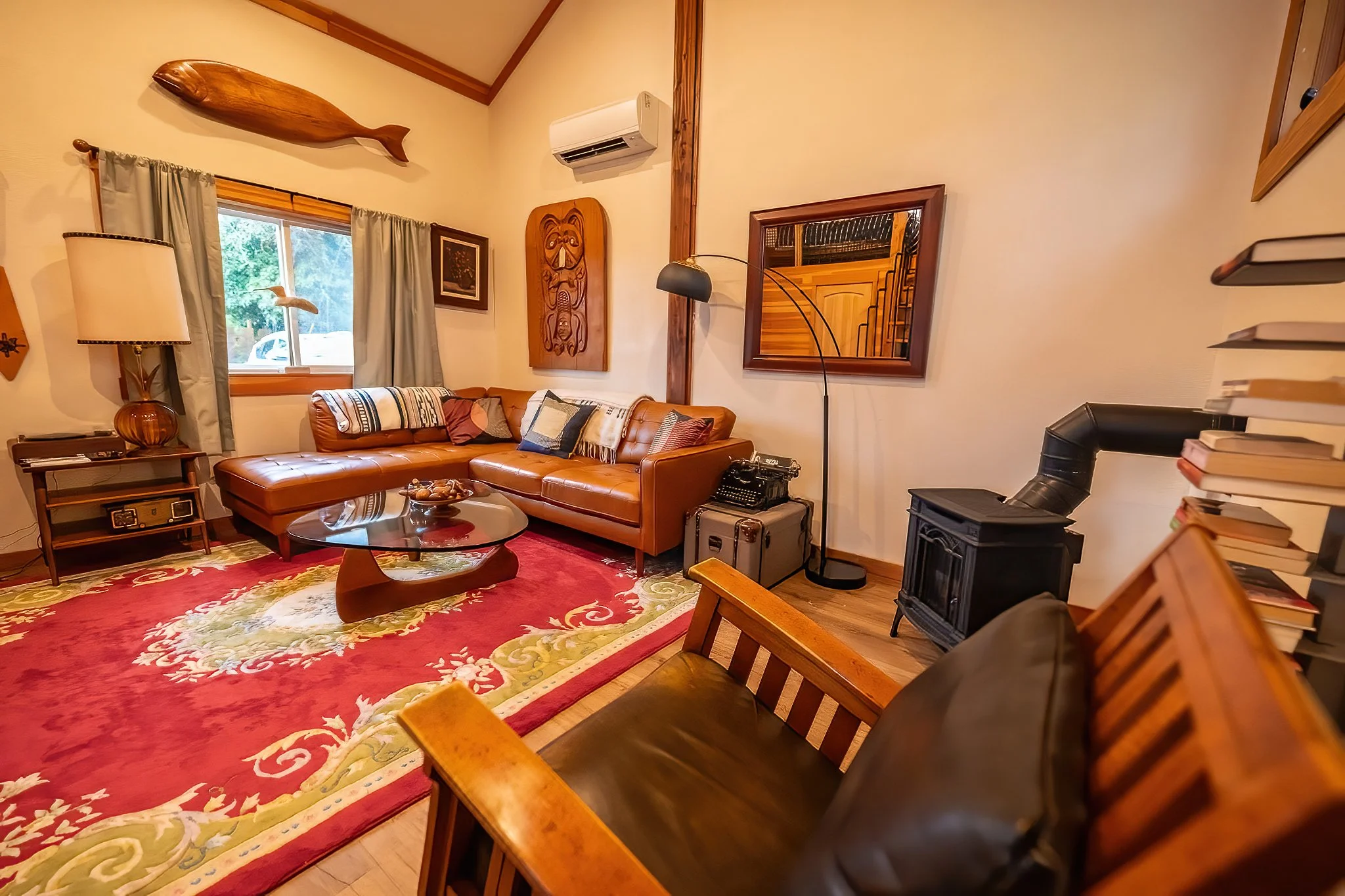 Living room with a leather sofa, a wooden coffee table, a red patterned rug, a fireplace, a bookshelf, window with curtains, and wall decorations.