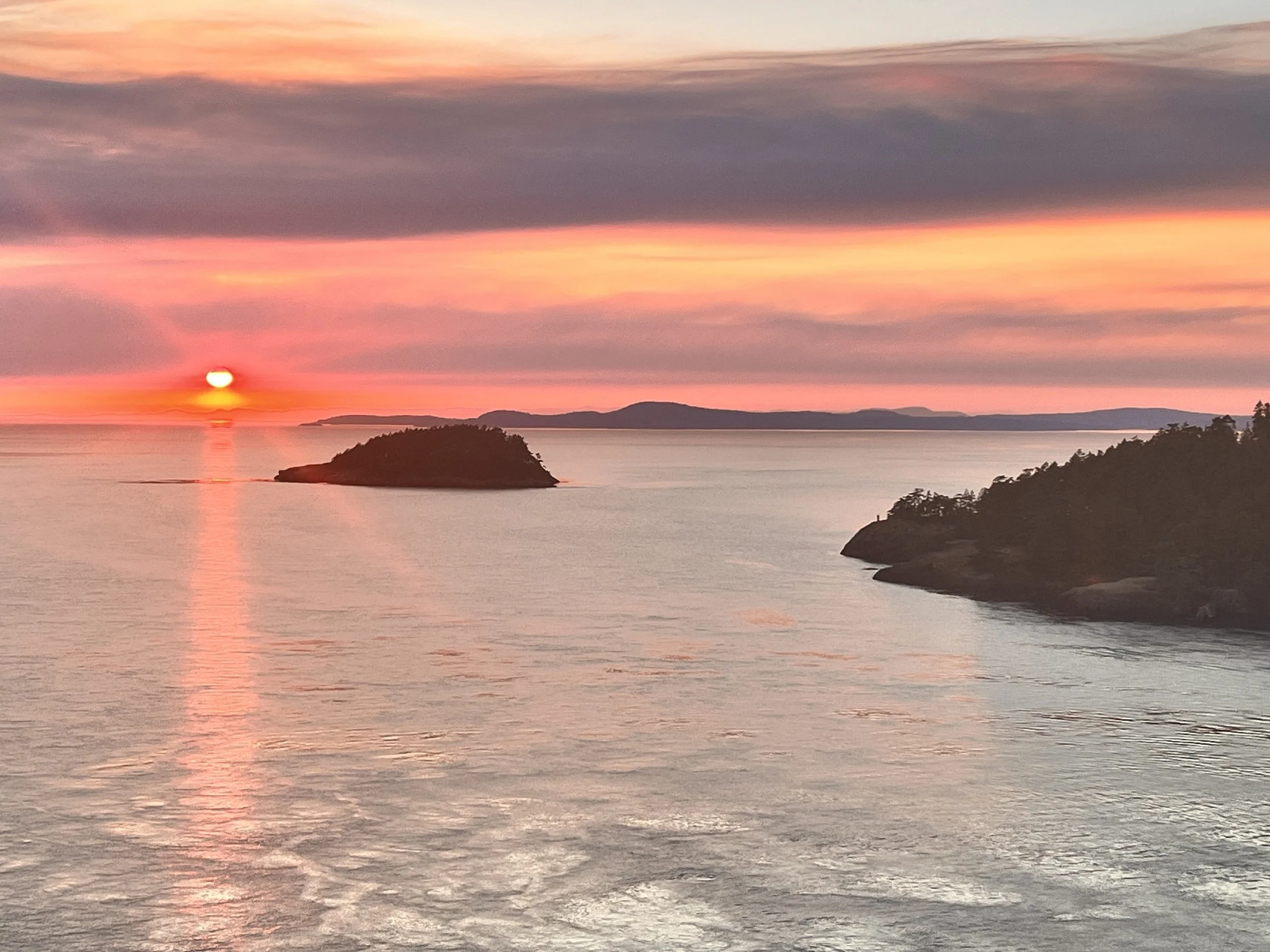 Sunset over a calm sea with small islands and a partly cloudy sky.