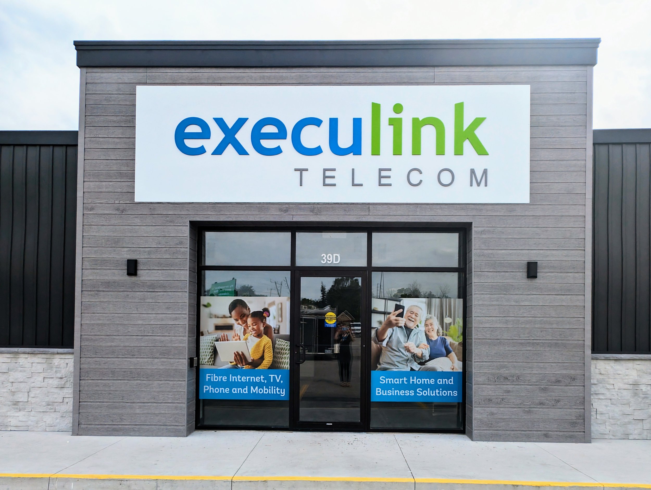 Storefront of Execulink Telecom showing signage and promotional images. The signs read "Fibre Internet, TV, Phone and Mobility" and "Smart Home and Business Solutions."