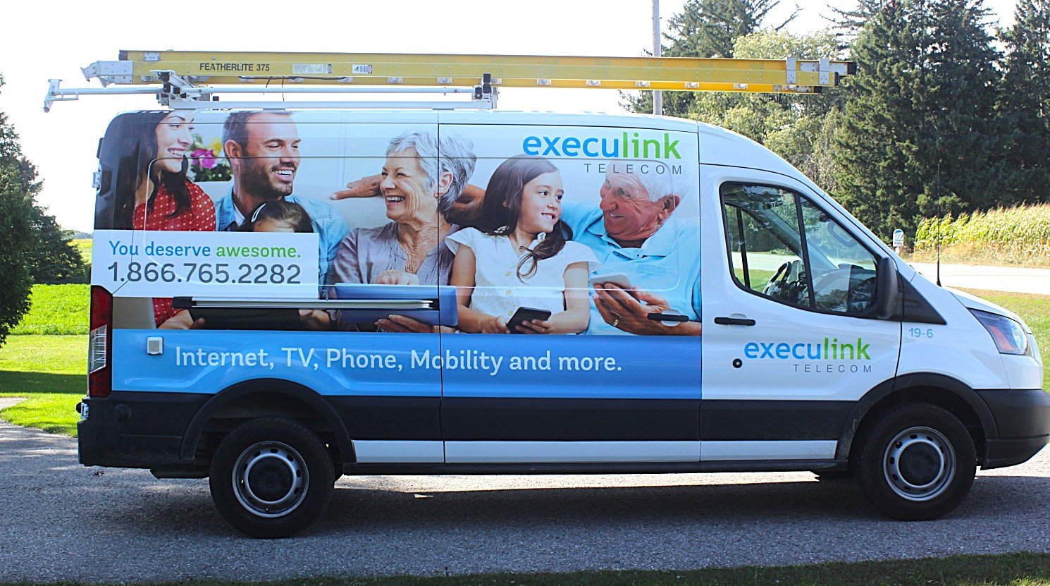 White van with "Execulink Telecom" branding and images of smiling people using digital devices. Ladder mounted on the roof. Offers Internet, TV, phone, and mobility services. Phone number displayed on the side.